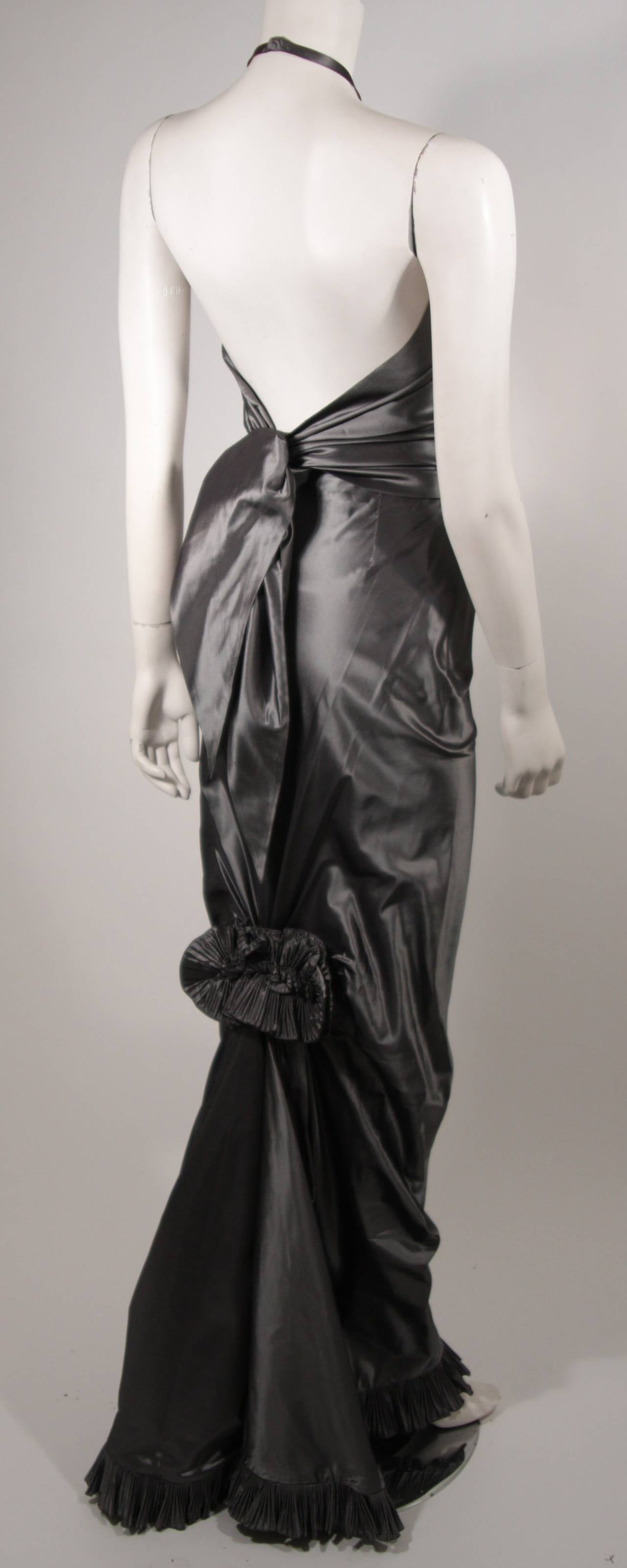 Ce superbe ensemble de soirée Oscar De La Renta est composé d'un magnifique tissu métallisé argenté. Le dos nu est agrémenté d'une cravate surdimensionnée. La jupe présente une coupe étroite, accentuée au genou par un volant floral qui se termine