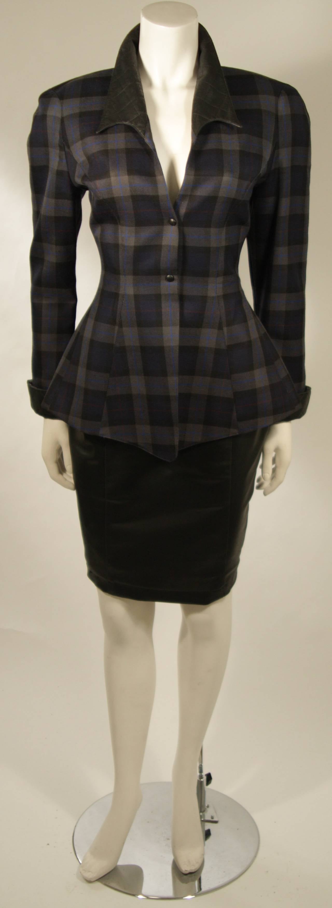This Thierry Mugler two-piece skirt suit is composed of a blue and grey plaid with faux leather. The jacket is accented by a quilted faux leather at the collar and cuffs. The skirt is composed of a black faux leather and features a pencil silhouette