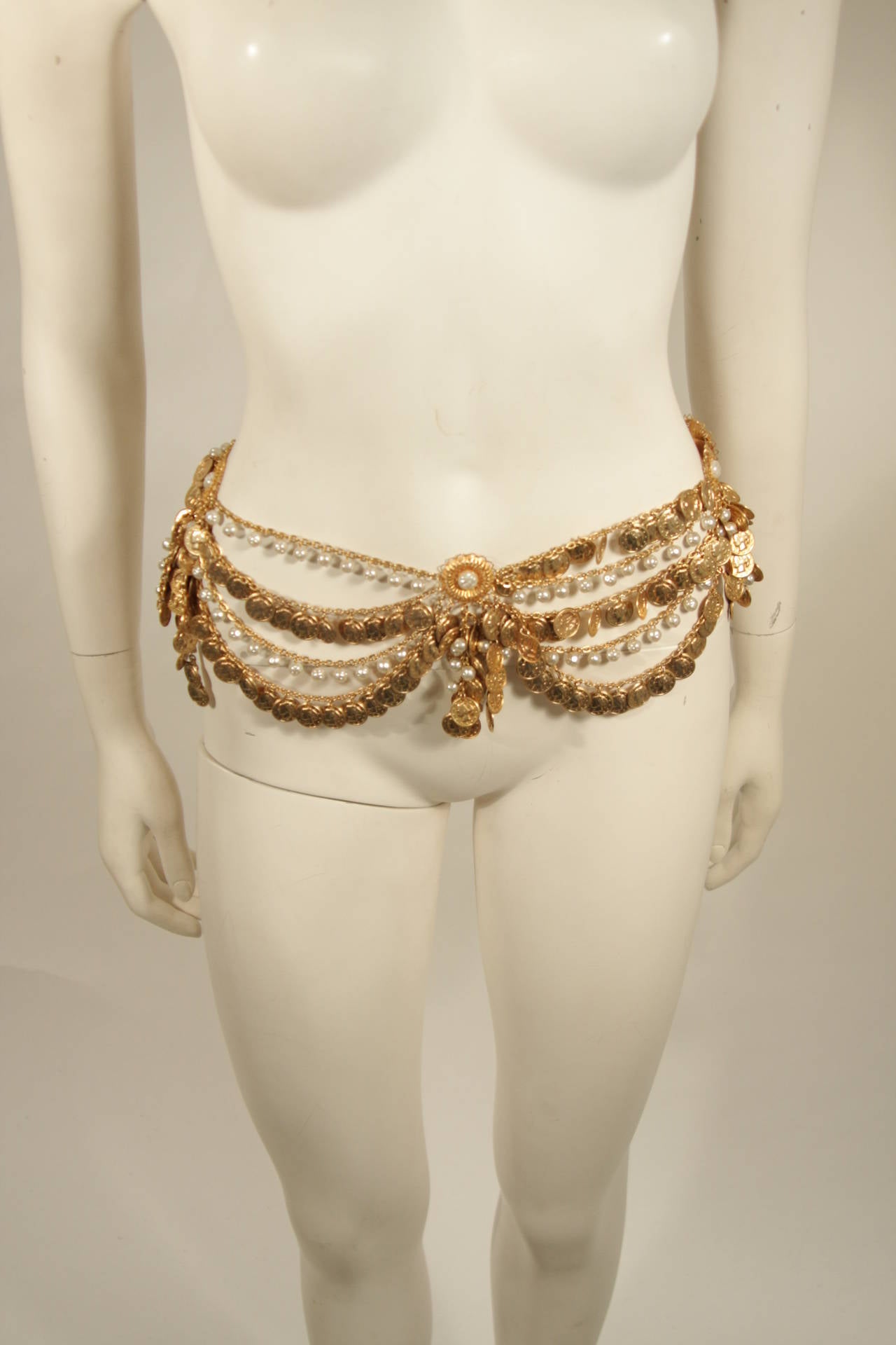 This Chrisitian Dior design is available for viewing at our Beverly Hills Boutique. The belt is a gold hue with gold coins and faux pearl adornments. Features a hook closure. Measures (approximately) 26.5