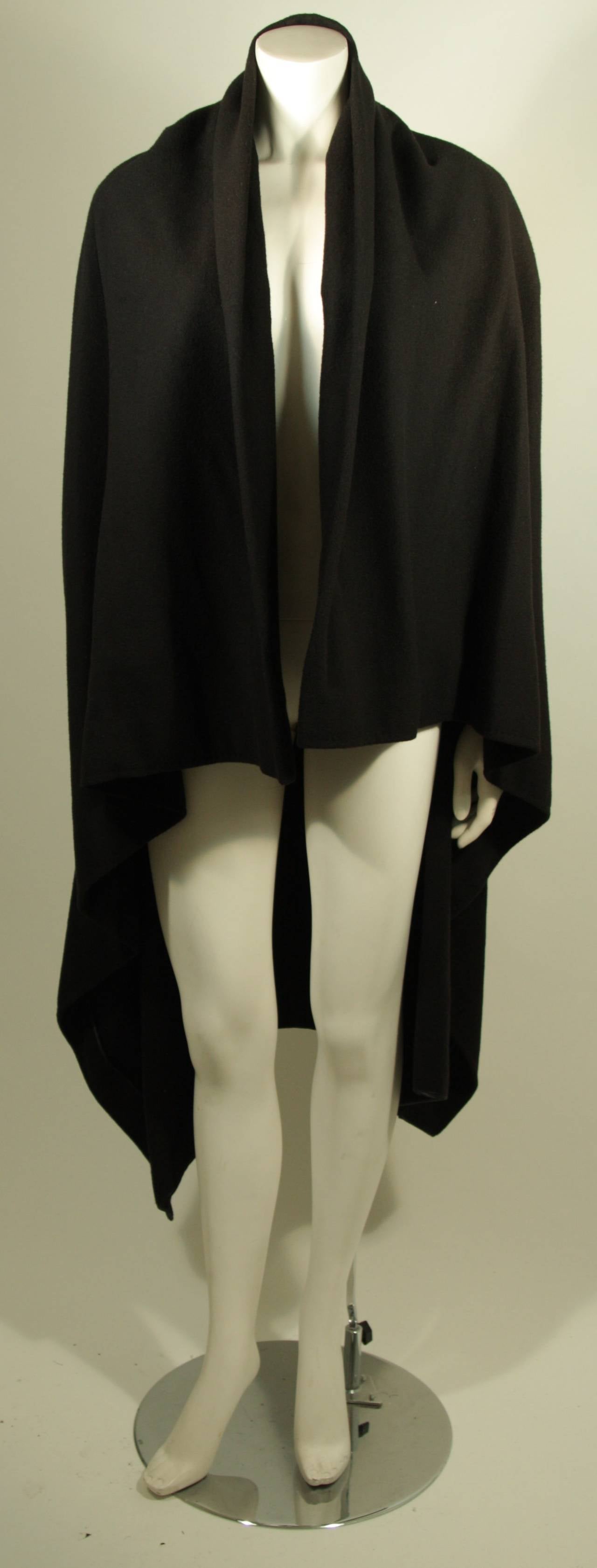 This Maison Martin Margiela original is available for viewing at our Beverly Hills Boutique. The cape style coat is composed of a black wool. It is a throw styl which can be wrapped and adorned with a brooch as a closure. Silk lining. There are very