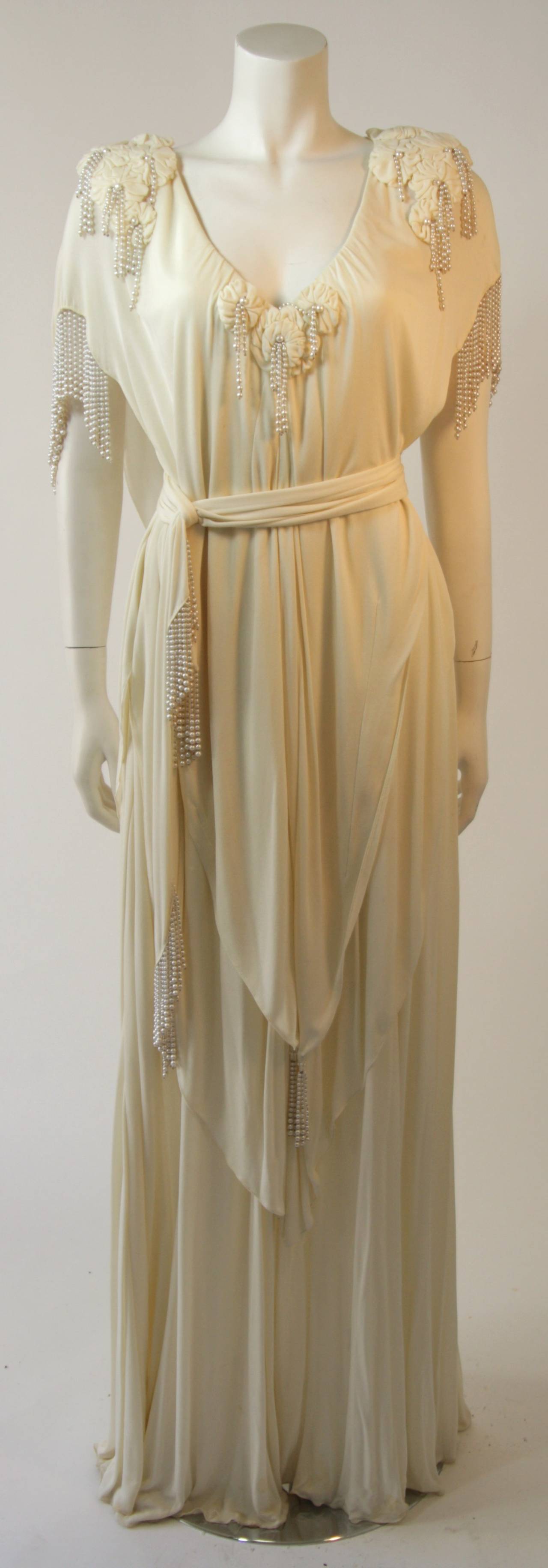 This stunning Holly's Harp design is available for viewing at our Beverly Hills Boutique. This gown is composed of an off white jersey and is accented with pearls. The kaftan style design comes with a belt for a contouring of the waist. A stunning