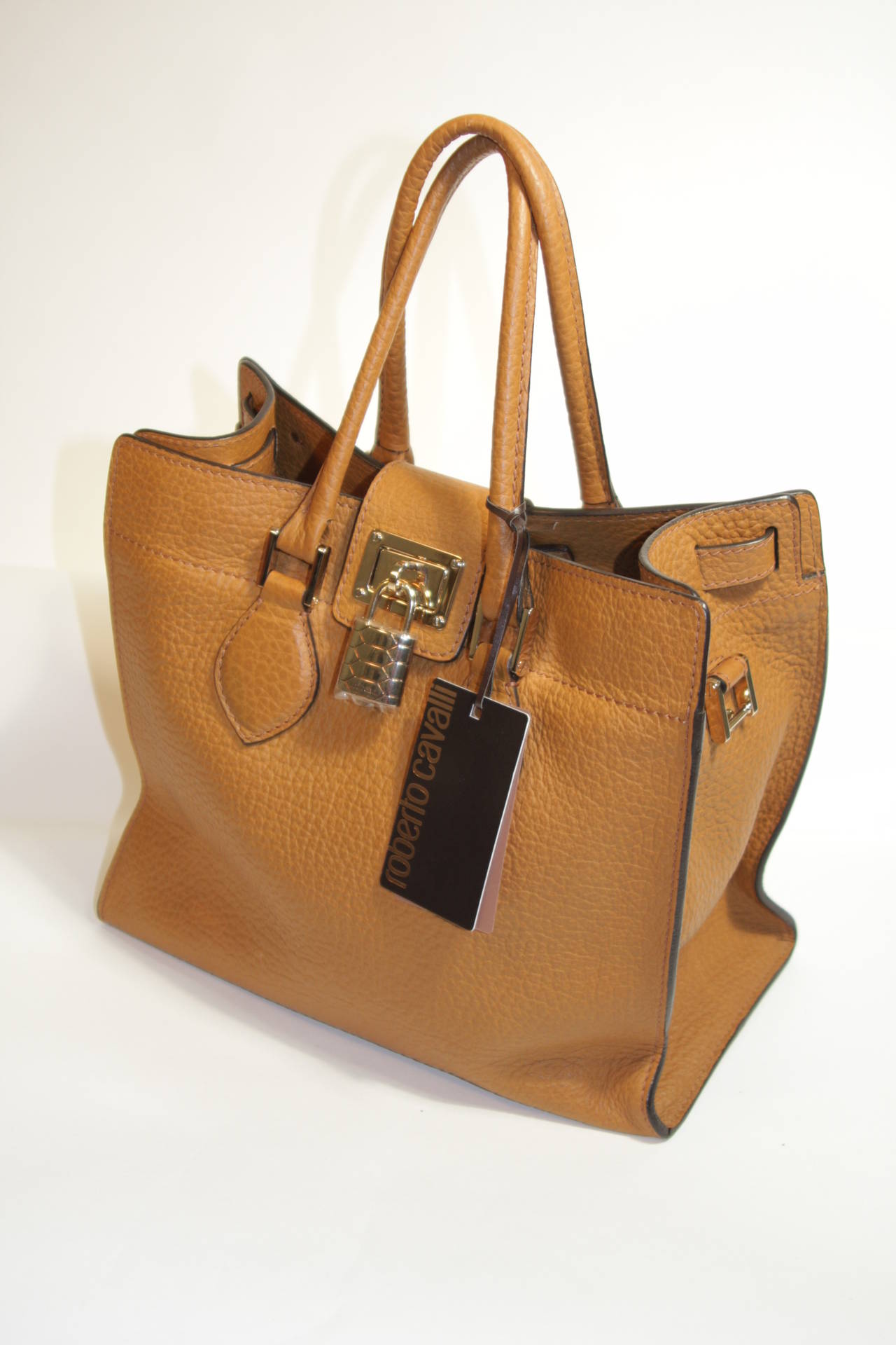 This Roberto Cavalli purse is composed of the finest leather in a wonderful tan hue. There are double double strap handles and a zipper closure. The purse is in excellent condition, possibly unused. Comes with dust bag. Missing strap. The interior
