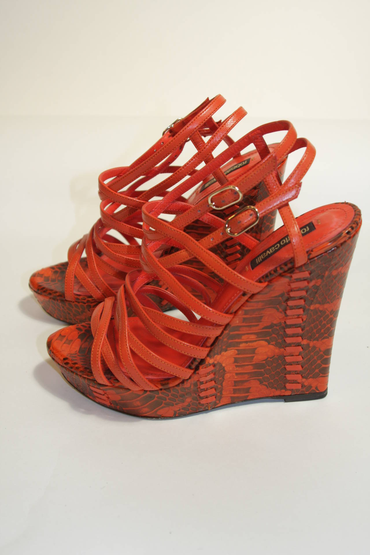 These Roberto Cavalli wedges are in excellent condition and only feature slight wear on the soles, worn less than a handful of times. They are composed of orange snakeskin and leather. Multi-strap design with dual buckles and slim cut wedge. Comes