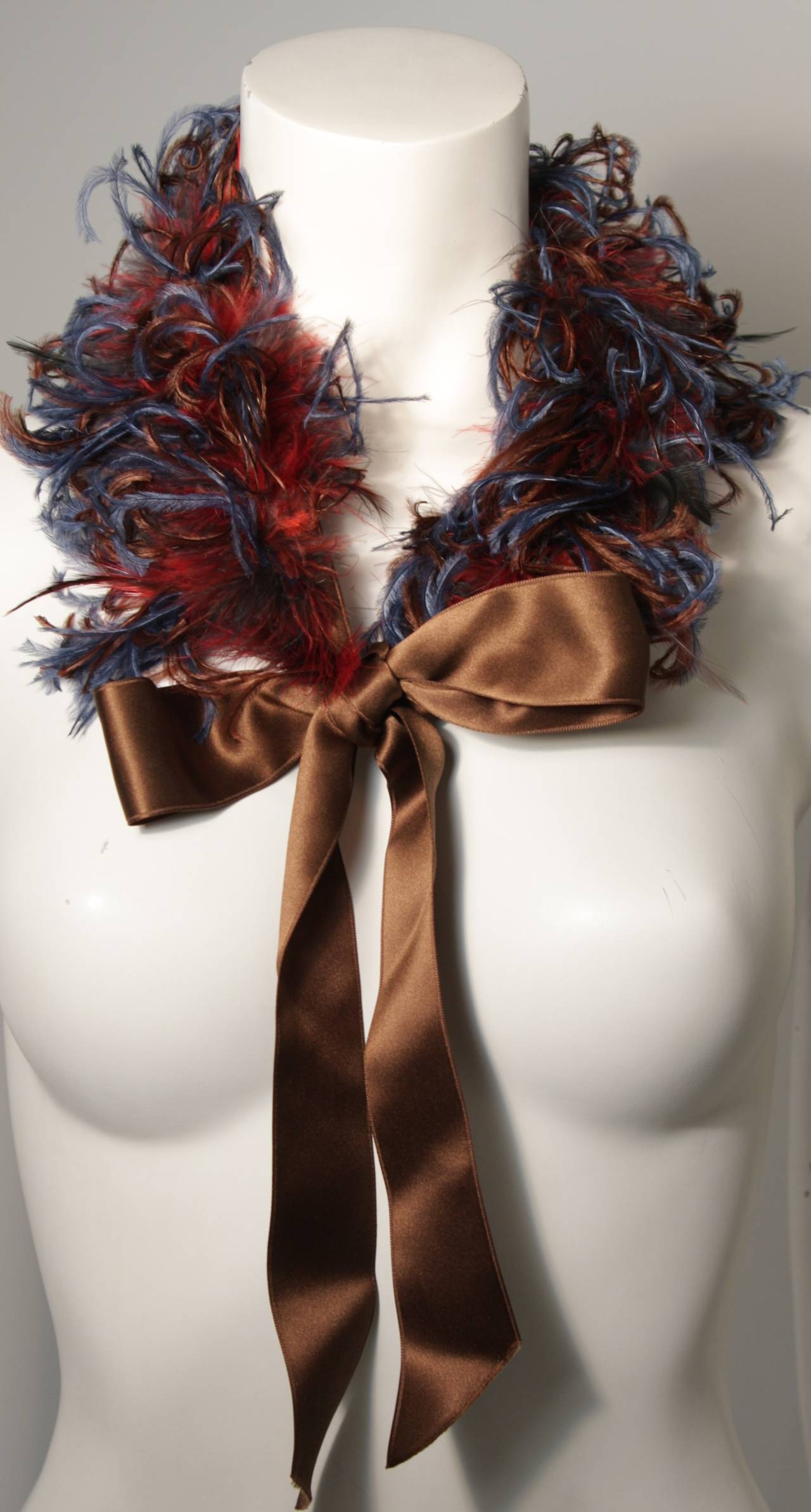 This Yves Saint Laurent design is available for viewing at our Beverly Hills Boutique. The base is a brown silk ribbon and the feathers are a blue and red hue. Made in France. With original tag. 

Please feel free to contact us with any inquiries.