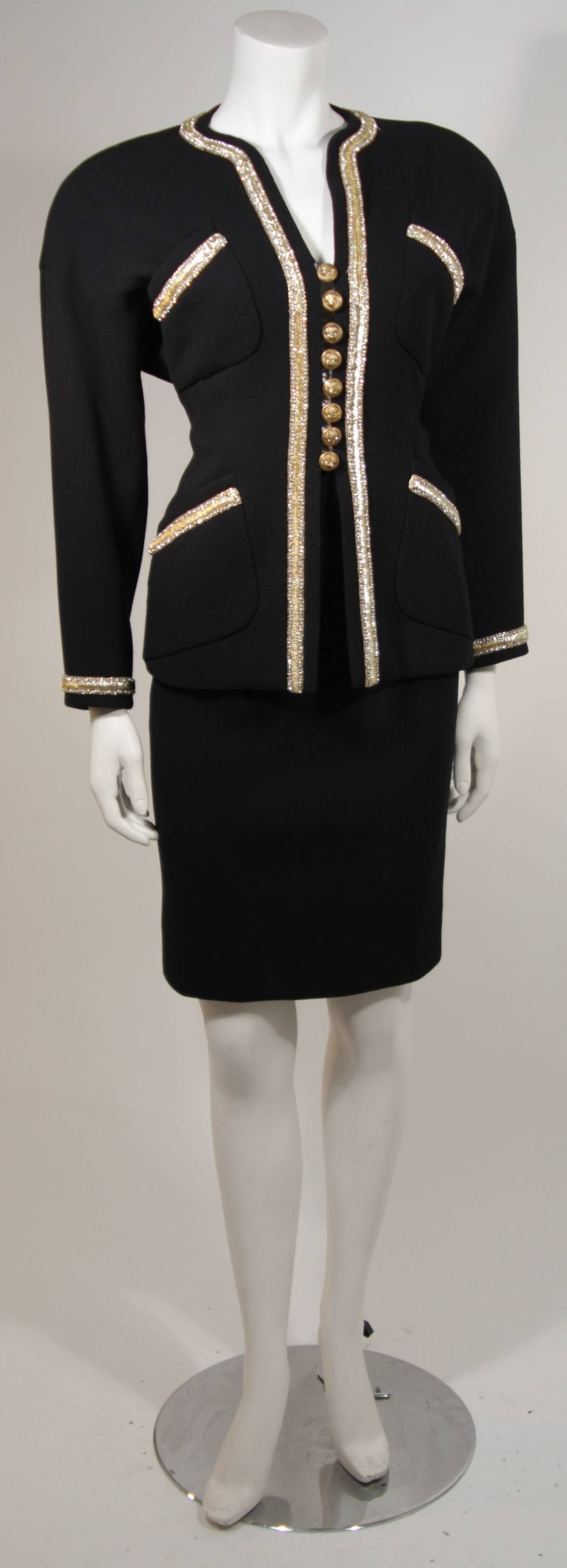 This Chanel suit is available for viewing at our Beverly Hills Boutique. The skirt suit is composed of a black wool and silk lining.The set is accented with a gold beaded trim and owl design buttons. The jacket has four front pockets and center