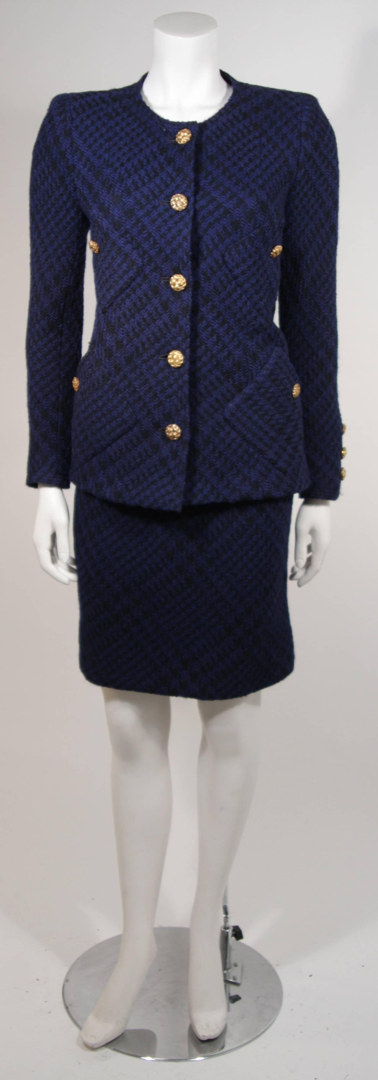This Chanel suit is available for viewing at our Beverly Hills Boutique. The suit is a two piece ensemble which features a jacket and skirt. It is composed of a blue and black patterned tweed and lined with silk. The jacket features five center