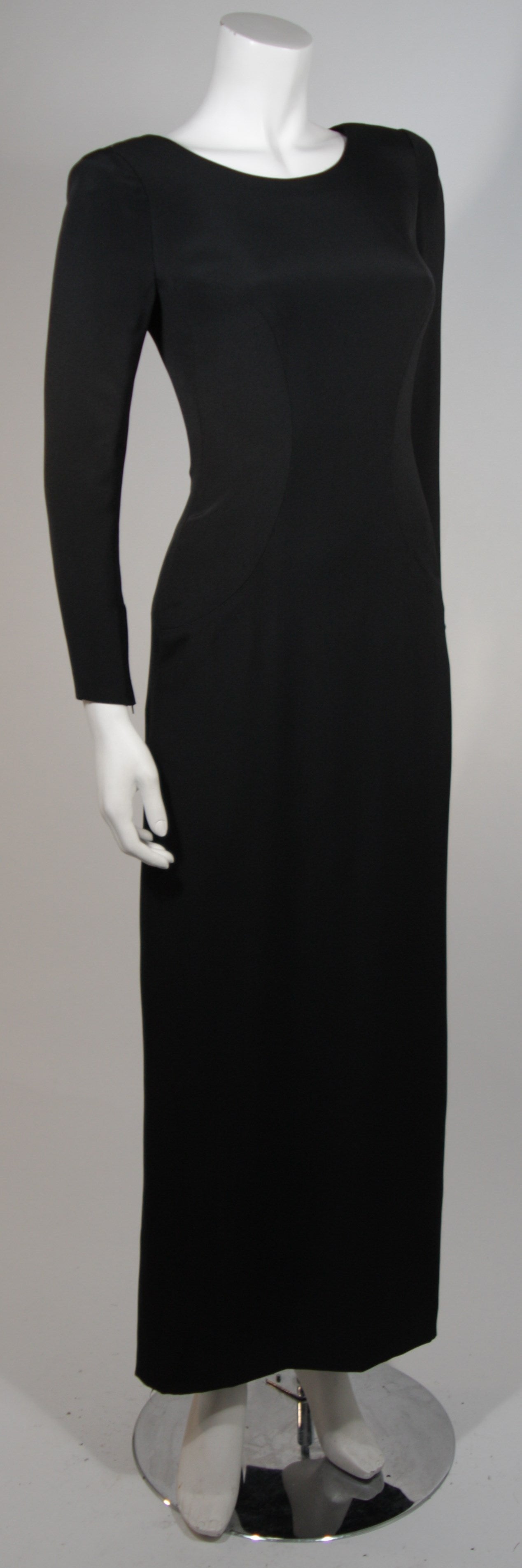 This Chanel gown is available for viewing at our Beverly Hills Boutique. The gown is composed of a black silk crepe. There is a v-back design with buttons and zippers at the wrists. The shoulders are padded. Garment is numbered. Made in France.