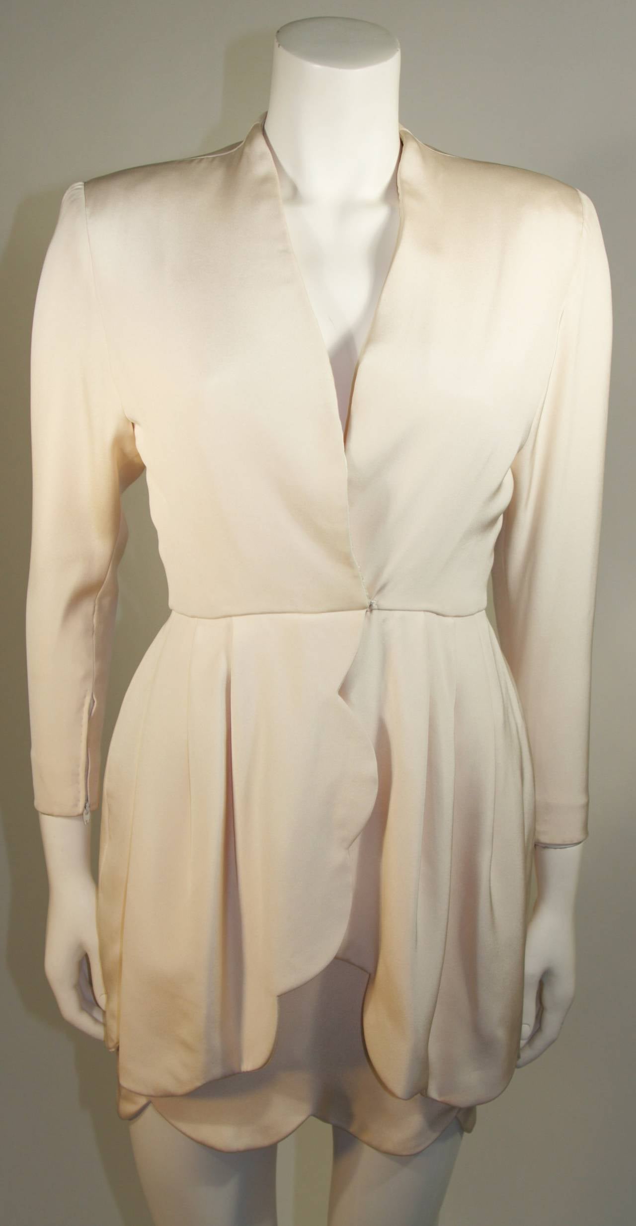 Cette robe est attribuée à JAMES GALANOS pour la boutique Ira Berg. La robe est en soie crème avec un large bord festonné décoratif. 
La fermeture se fait au centre du devant, avec une fermeture à glissière et un crochet. Les manches sont également