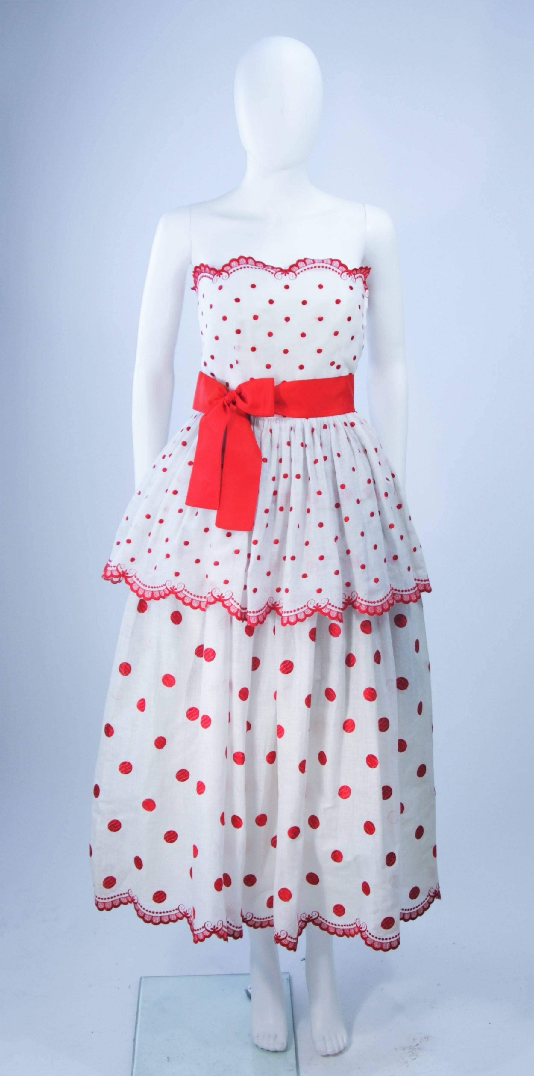  This Alberto Capraro dress is composed of a white fabric embroidered with red. The tiered design features scalloped edging. There is a zipper closure and ribbon belt. In excellent vintage condition. 

**Please cross-reference measurements for