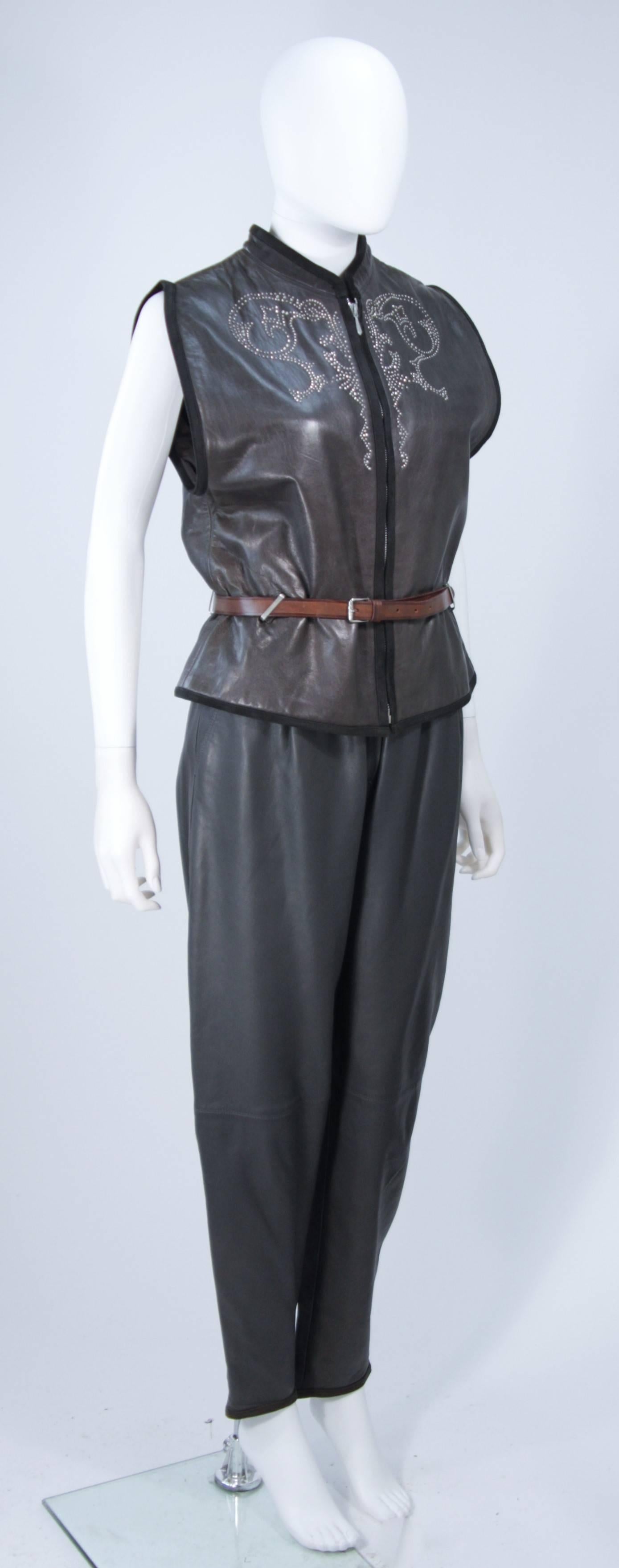  This Versace ensemble is composed of a grey leather and has suede accents with metal studs. The vest features a center front zipper closure with a belt. The trousers have a pleated front and side pockets with a belt. In excellent vintage