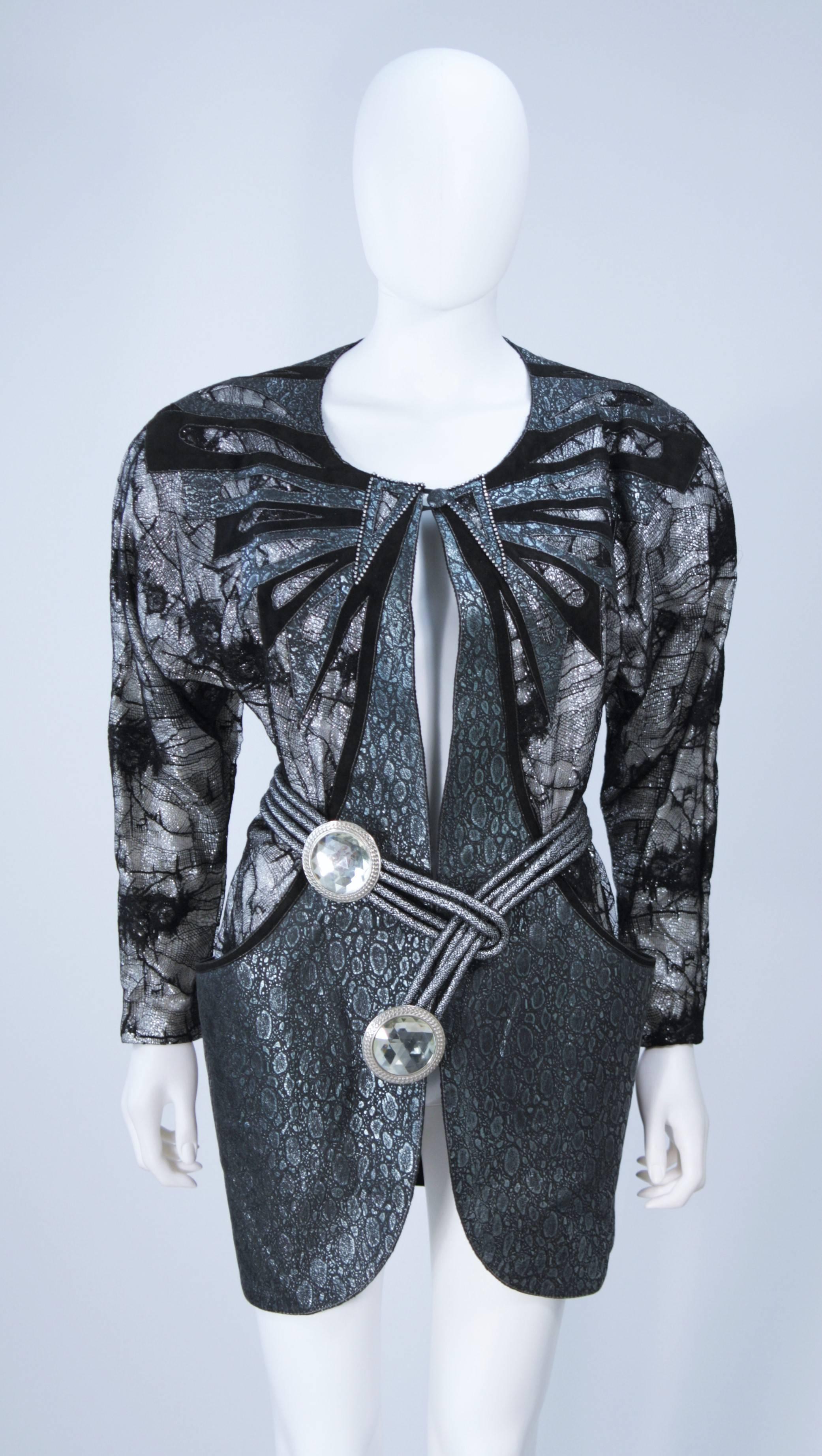  This Roberto Cavalli jacket is composed of a metallic lace and suede combination. Features a center front button closure, shoulder pads, and side pockets. There is a large jeweled belt with silver hue metal. In excellent vintage