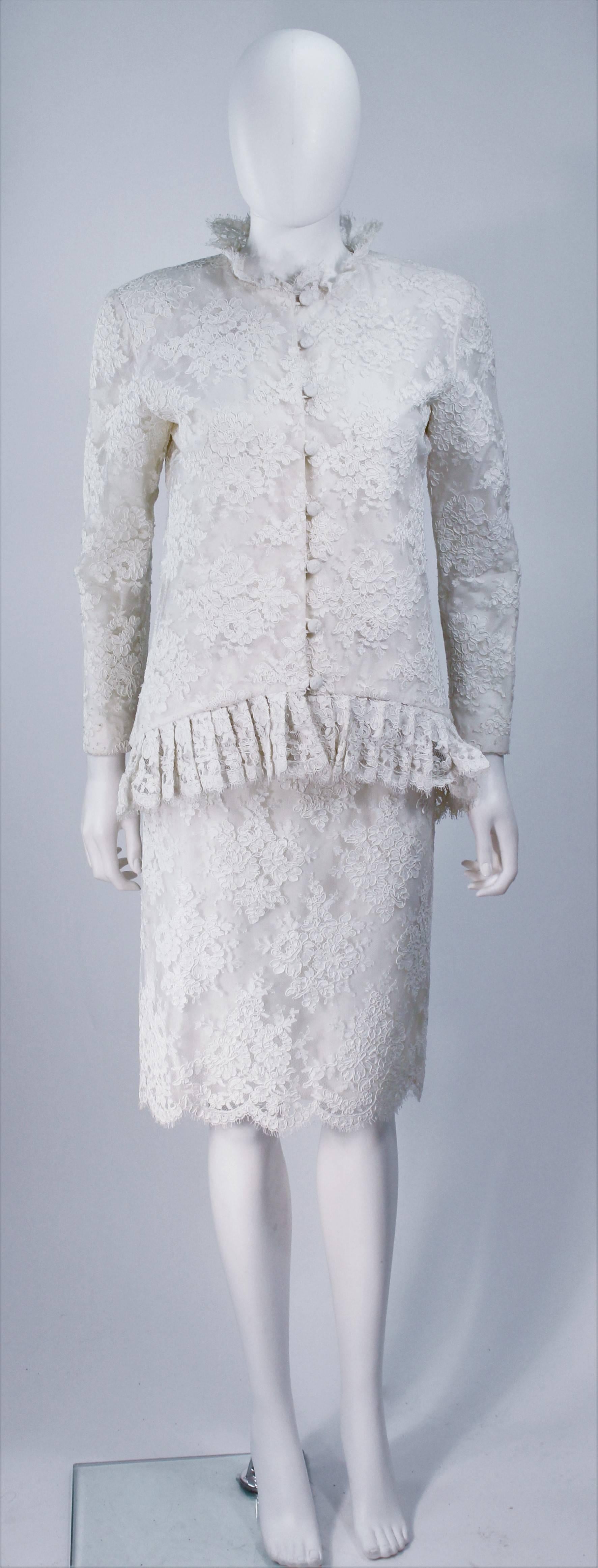  Cet ensemble Bon Choix est composé d'une dentelle blanche aux bords festonnés. La veste  comporte des fermetures à boutons au centre du devant et un col à bord festonné. La jupe a un style crayon classique avec une fermeture à glissière. En