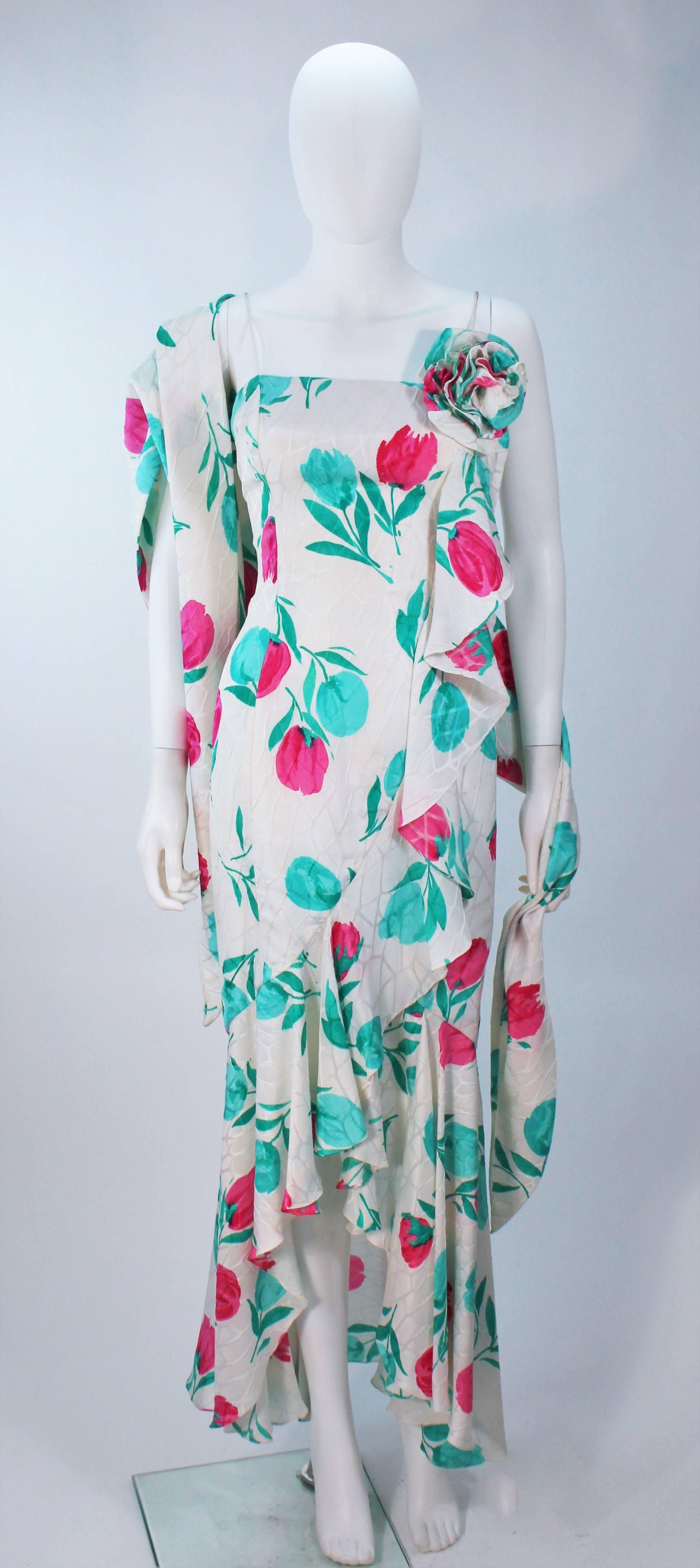  This Travilla gown is composed of an off-white silk with a turquoise and pink floral motif. Features a side draped ruffle with large flower. There is a center back zipper. Comes with wrap In excellent vintage condition. 

  **Please