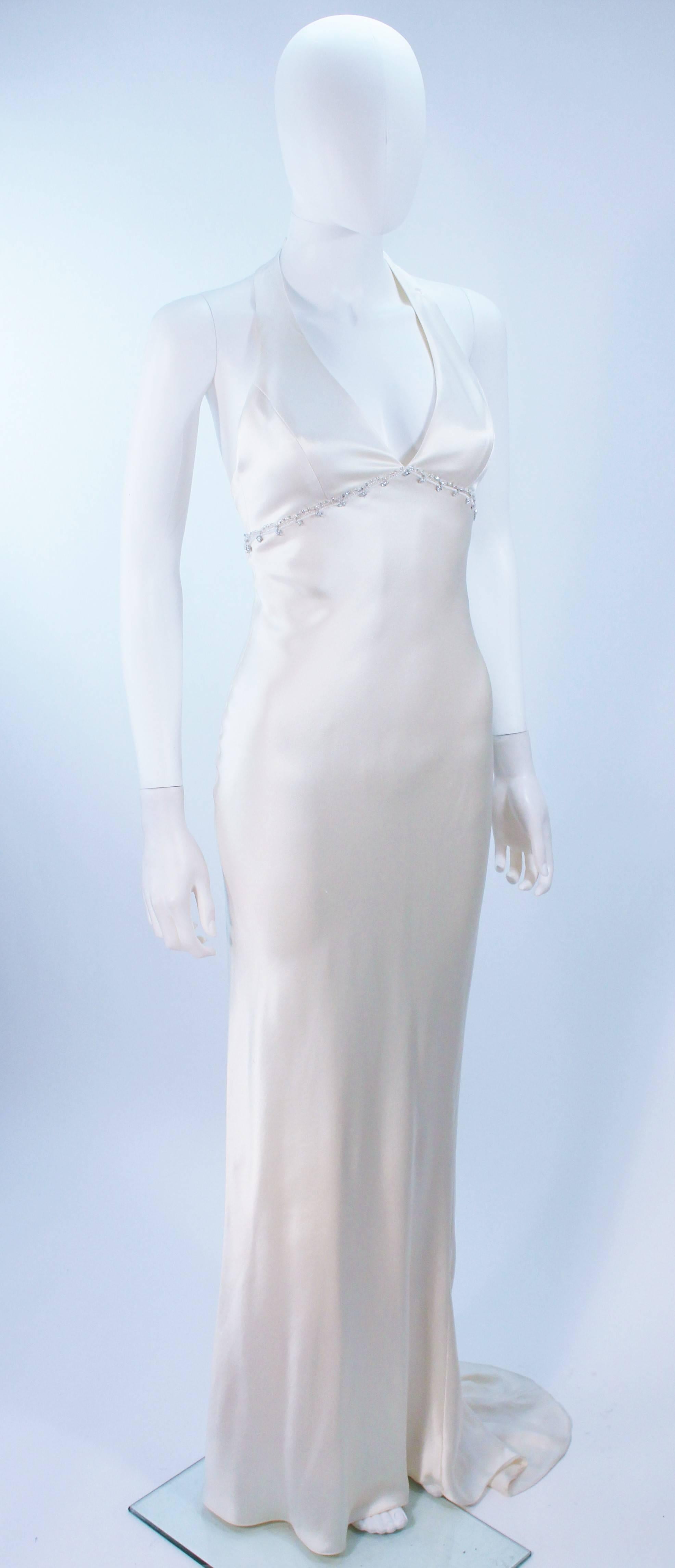  This Monique Lhuillier  gown is composed of a white bias cut silk and features a rhinestone applique at the empire waistline. There is a center back zipper closure, and train. In excellent vintage condition. 

  **Please cross-reference