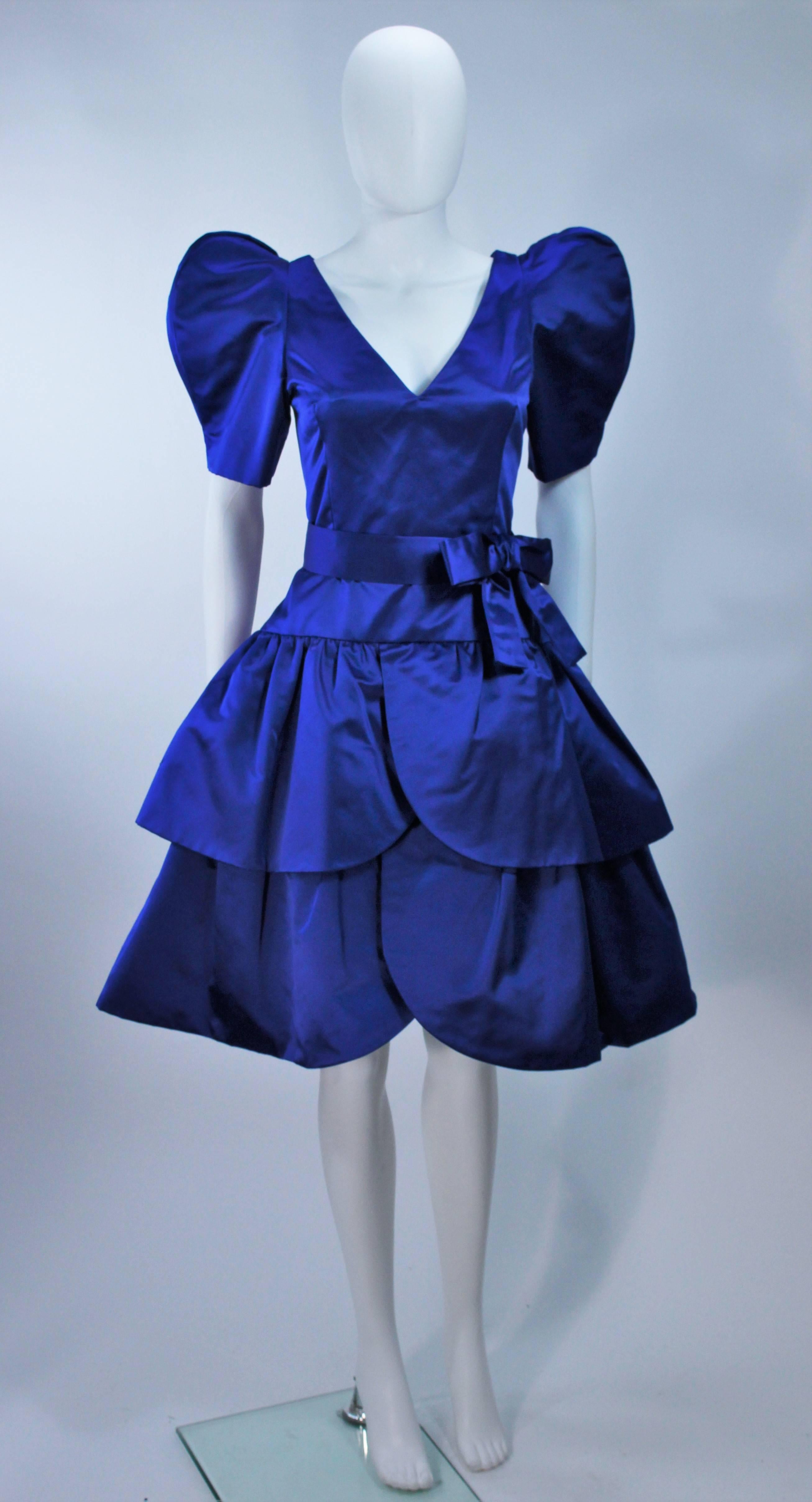  This Arnold Scaasi cocktail dress is composed of a blue satin combination with exaggerated sleeves and bow at waist. There is a center back zipper closure. In excellent vintage condition. 

  **Please cross-reference measurements for personal