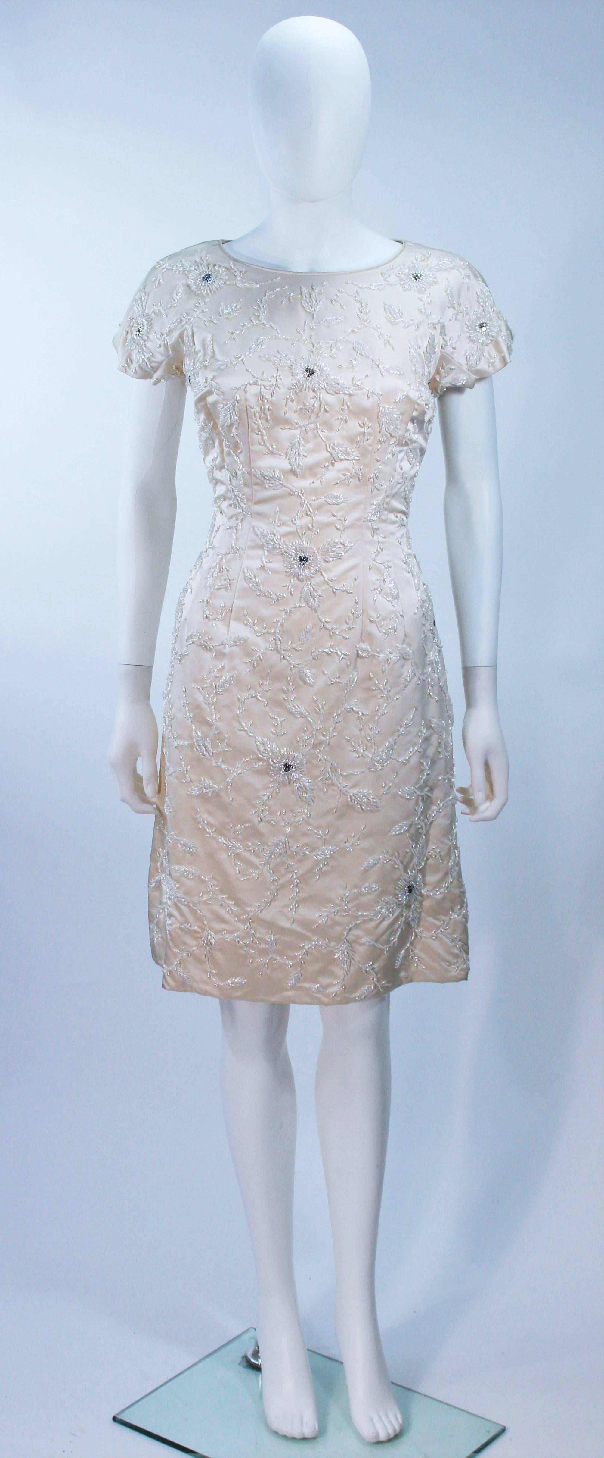  Cette robe de cocktail est composée d'une soie blanche (teinte ivoire) avec des perles et des manches courtes. Il y a une fermeture à glissière au centre du dos. Vintage, en excellent état. 

  **Veuillez croiser les mesures pour une précision