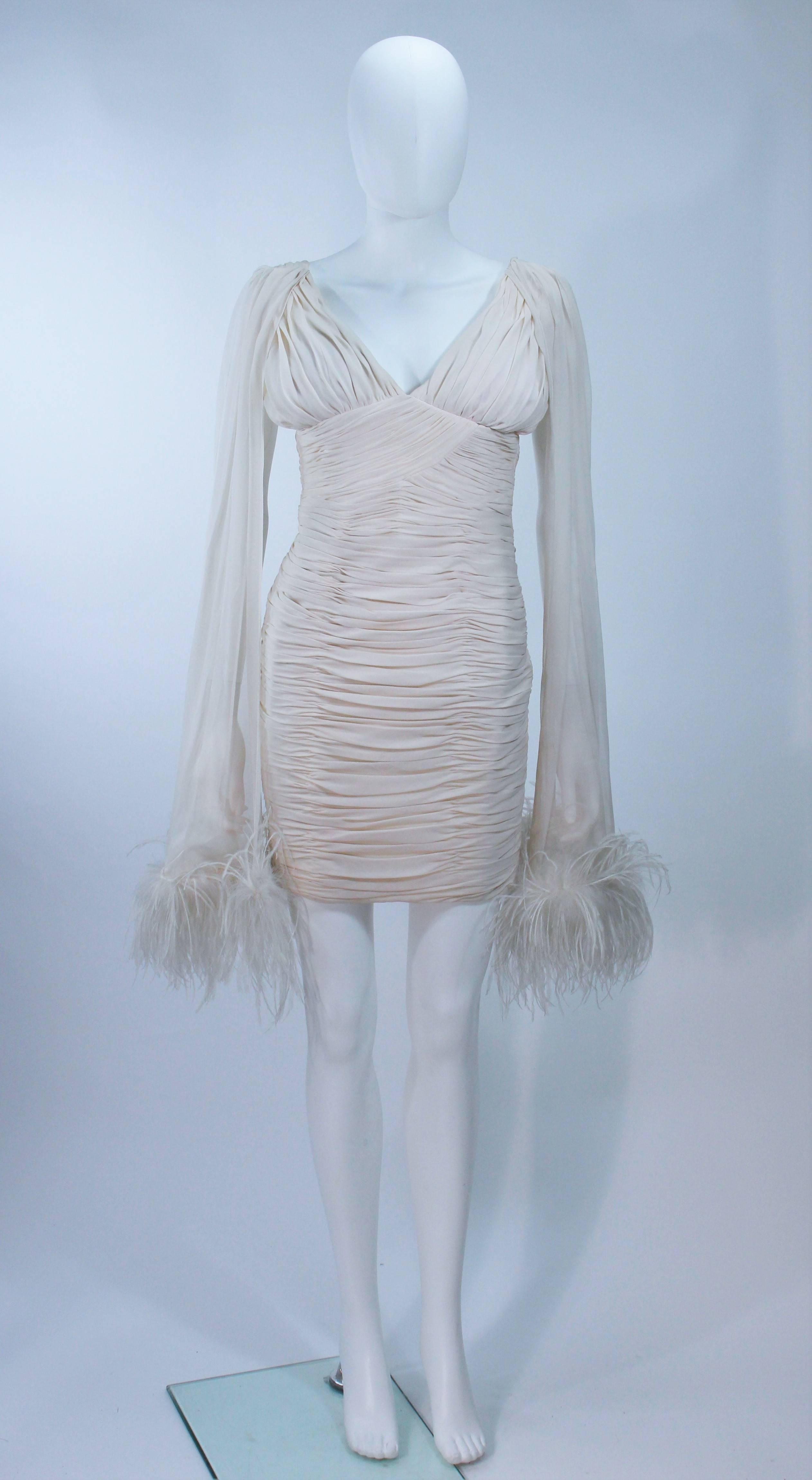  This vintage design is available for viewing at our Beverly Hills Boutique. We offer a large selection of evening gowns and luxury garments. 

 This cocktail dress is composed of a ruched white fabric with chiffon accents and feather applique.