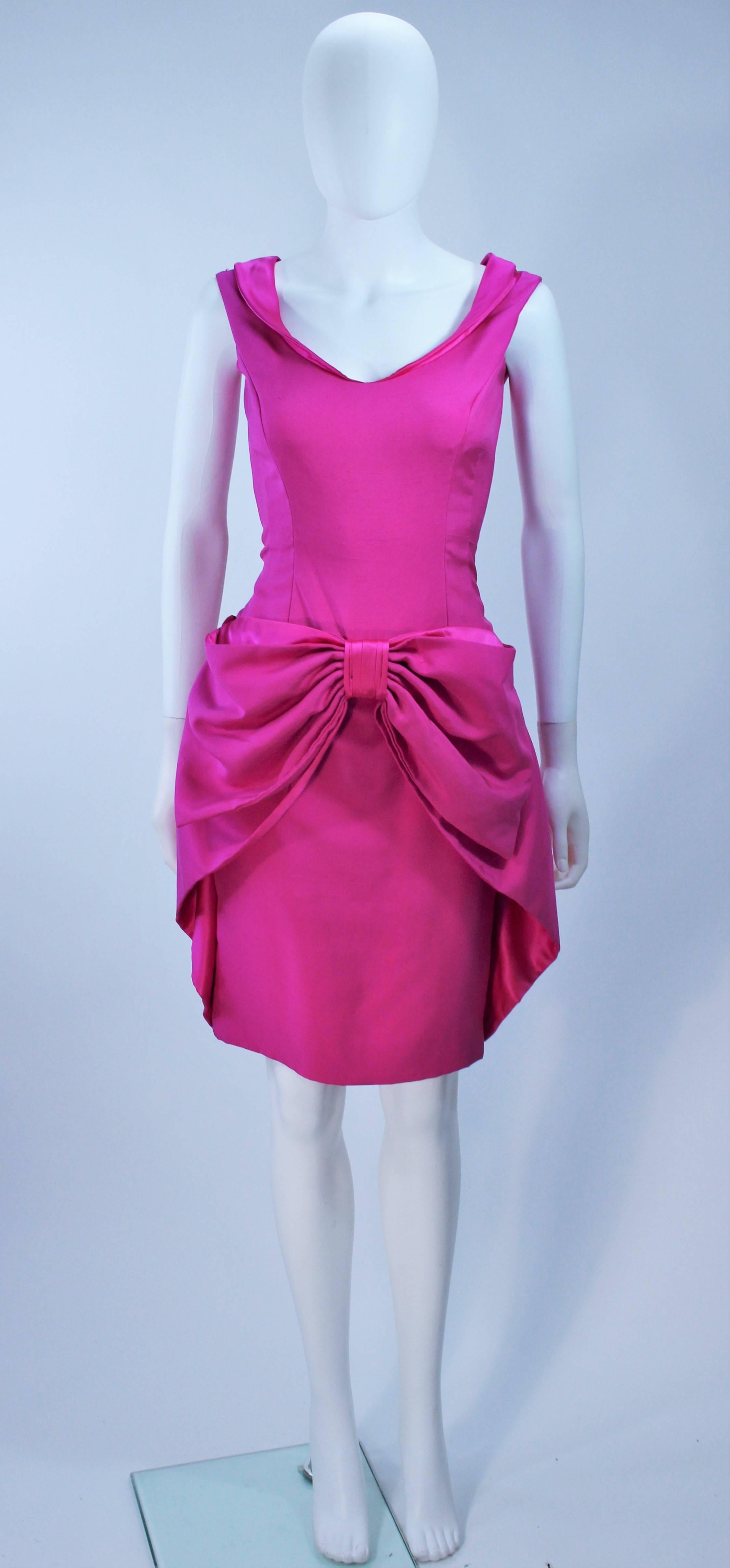 This Elizabeth Mason Couture pink silk dupioni sleeveless cocktail dress features a front draped bow with pockets. It is lined in silk satin and has a center back zipper. Made in Beverly Hills. 

This is a couture custom order. Please allow for a 60