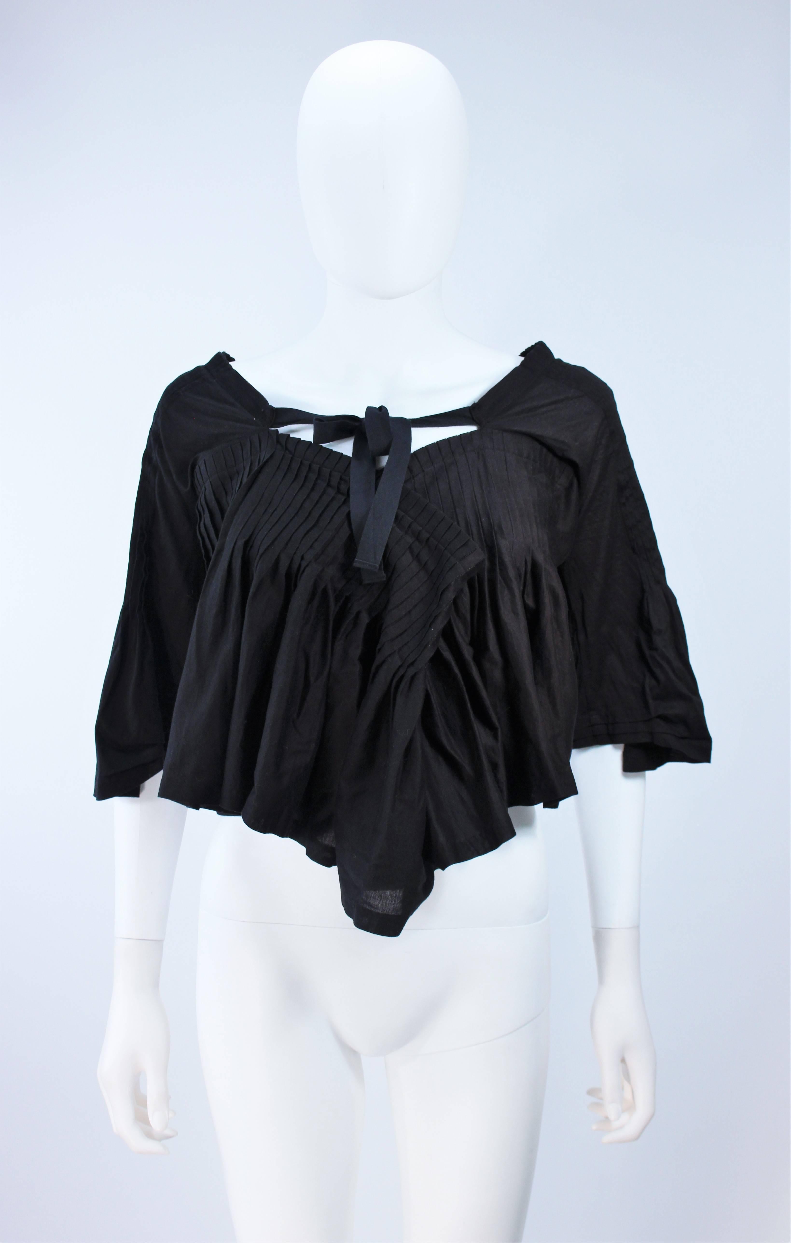  This Comme Des Garçons top is composed of a black pleated cotton with button detail at the center front and tie. In like new condition. 

  **Please cross-reference measurements for personal accuracy. 

Measures (Approximately)
Length: