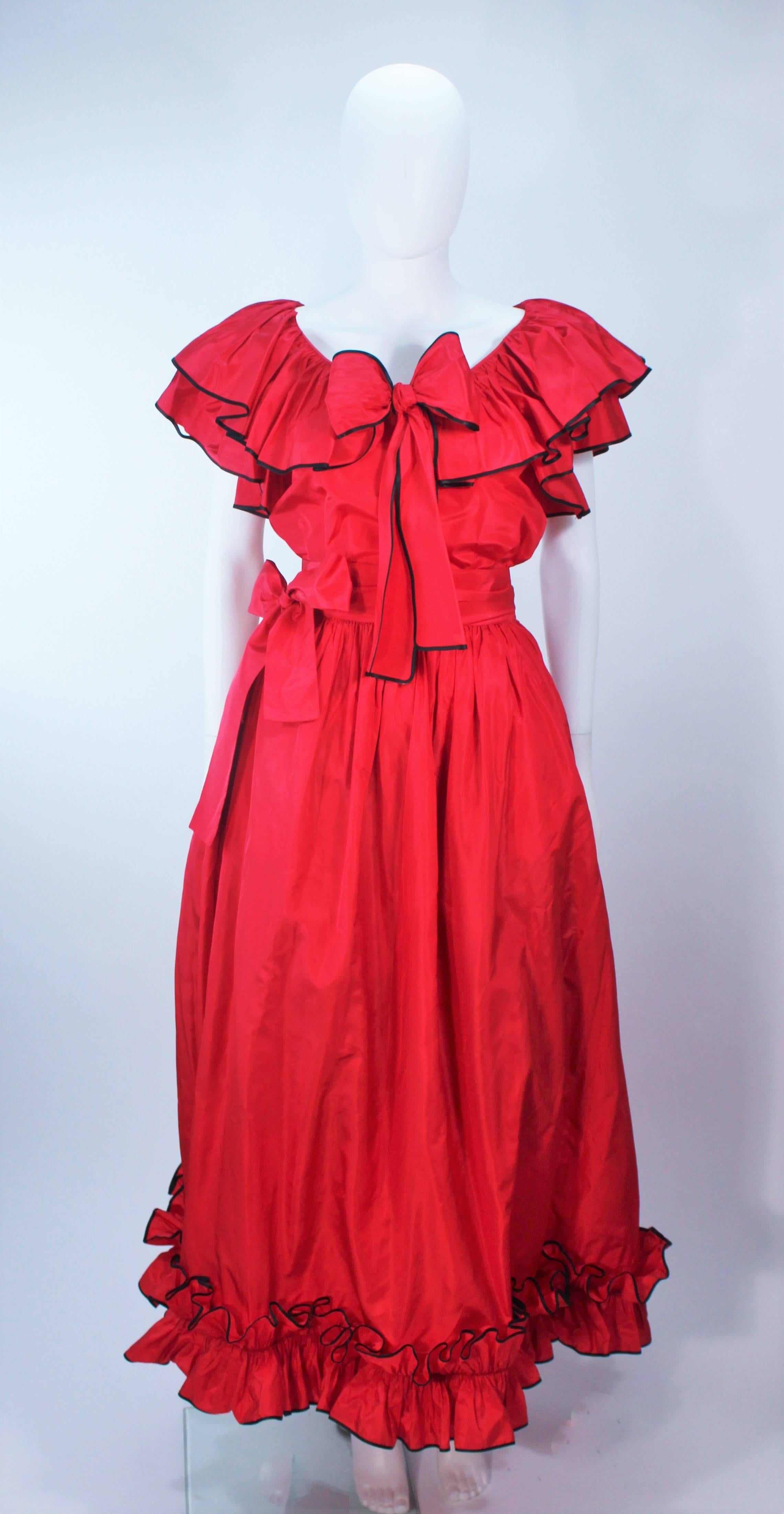 This Yves Saint Laurent  ensemble is composed of a red satin and features a ruffled trim with black. The ruffled blouse features a center front bow. The skirt was shot with crinoline and has a side zipper closure with pockets. Comes with belt. In