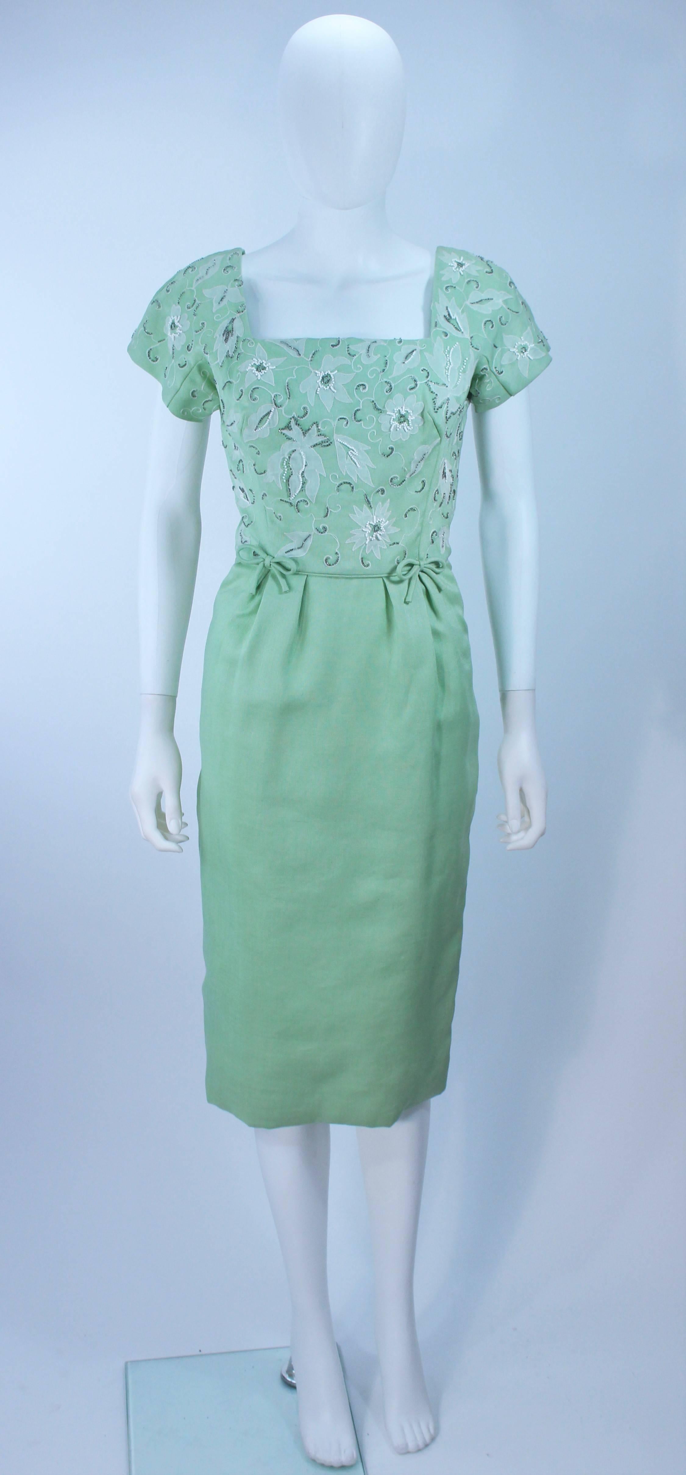  This dress is composed of a sage green silk or linen with white embroidery and beading. Features a scalloped edge design at the neckline, front bow details, and center back zipper closure. In excellent vintage condition.

  **Please