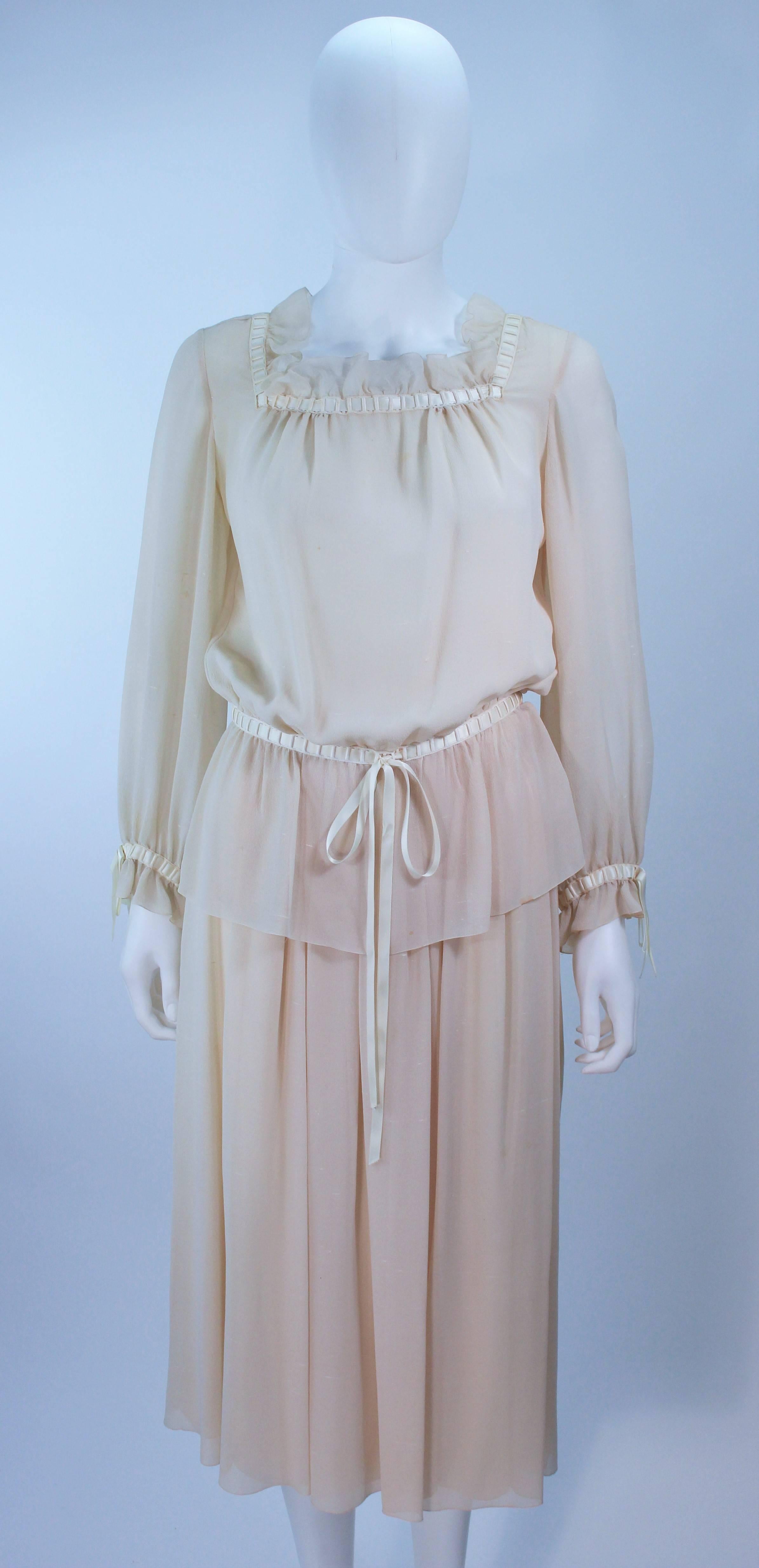 This Christian Dior Couture ensemble is composed of a raw silk chiffon in a natural nude hue. Features a peasant style blouse with ruffle and satin trim, there are side snap closures with hook and eyes. The skirt has a pleated style with side zipper