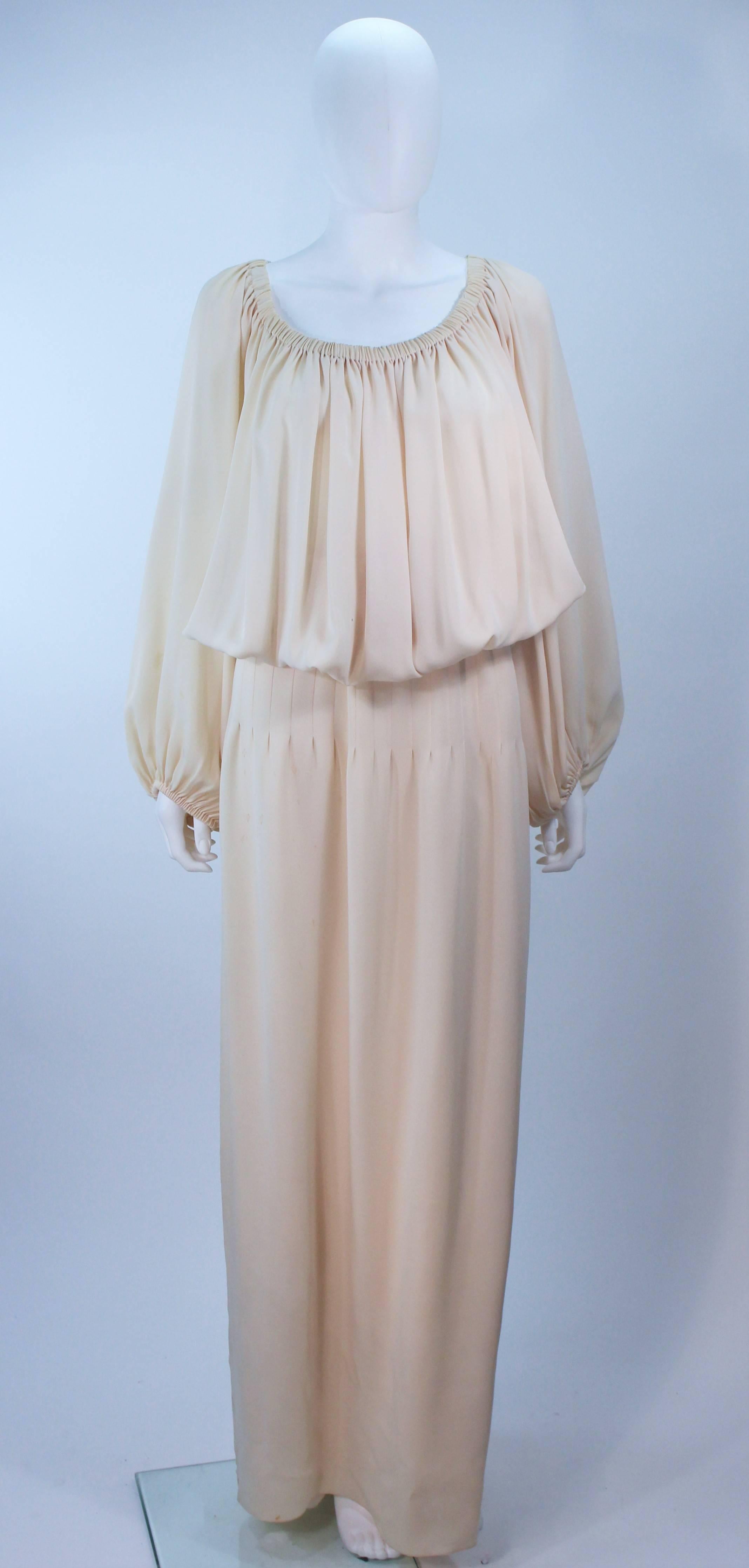 This Christian Dior gown is composed of a nude silk. Features and elastic neckline and sleeves with a pleated waist, which may be style on or off the shoulders. Comes with a slip skirt and waist belt. In vintage condition, (sold AS-IS) there is some