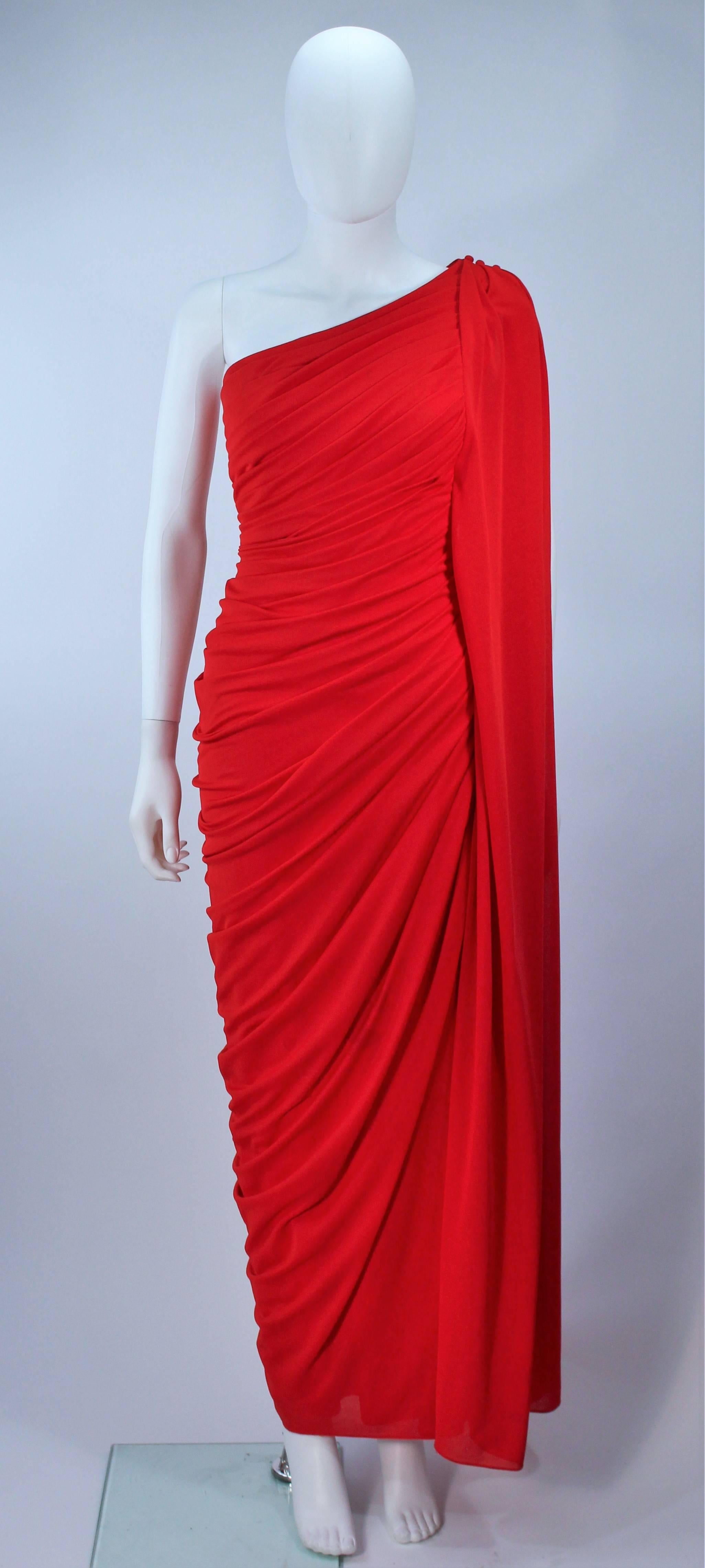 This Estevez  gown is composed of a red jersey. Features a gathered an draped design with side zipper closure, and button closures at the shoulder. In great vintage condition, excellent design. There is a spot on the front of the dress which may