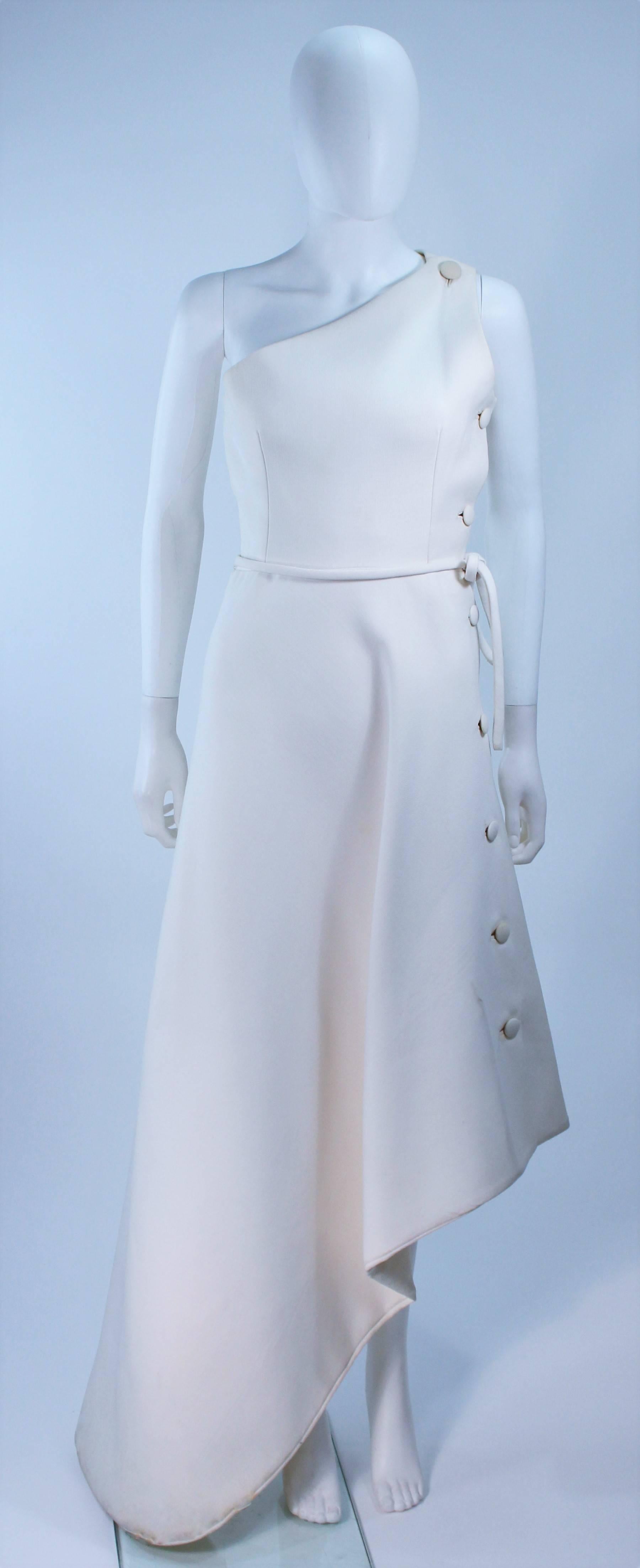 This Givenchy Haute Couture Gown is composed of a white wool and features an asymmetrical design with side button detail. In excellent vintage condition with some slight discoloration due to age.

Provenance:  Betsy Bloomingdale

Measures
Length: