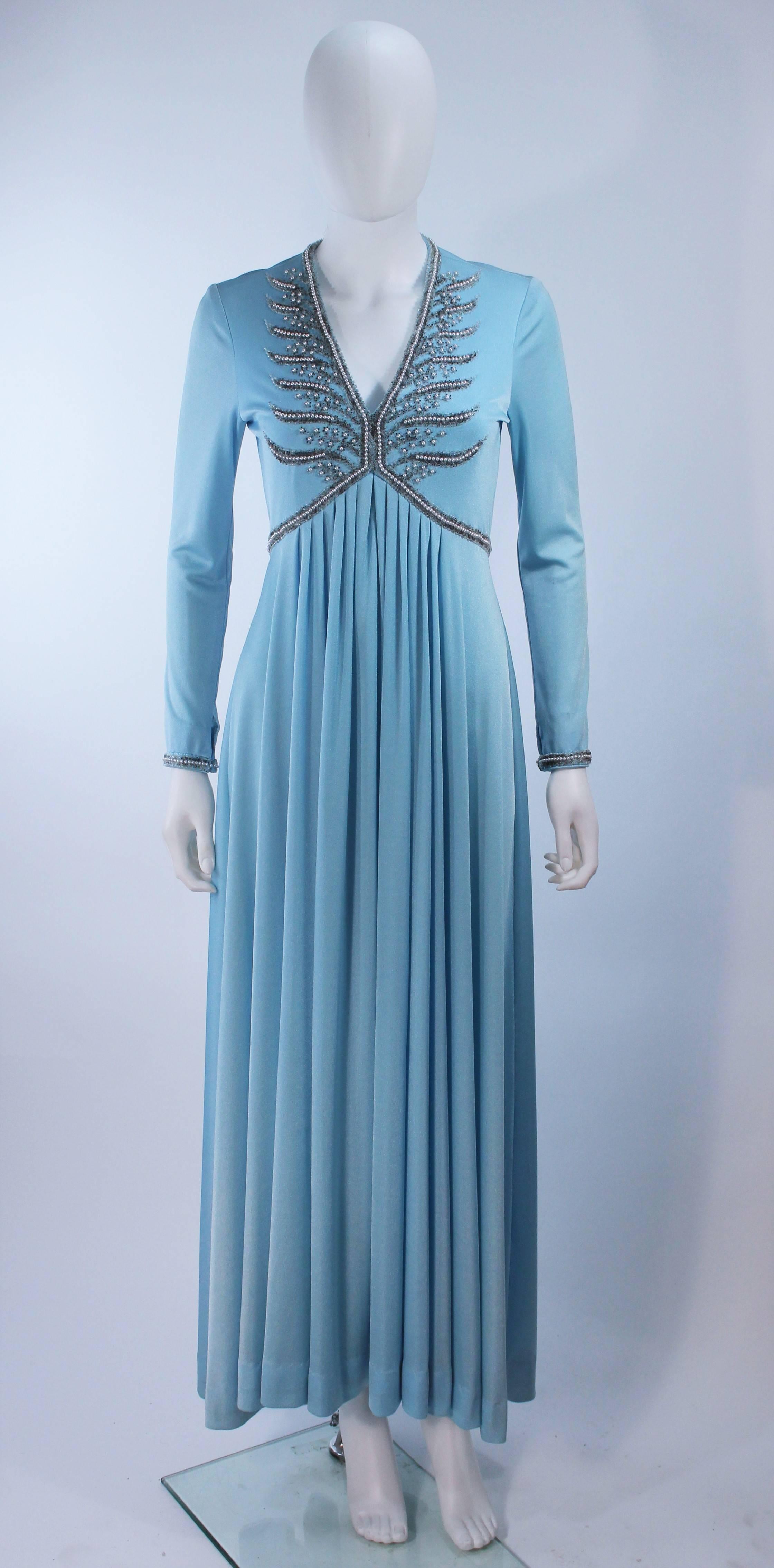 This gown is composed of a blue jersey with a beaded applique on the bust and sleeves. Features a draped design with a center back zipper closure, and hook & eyes at the sleeve end. In excellent vintage condition (there are some missing beads, but