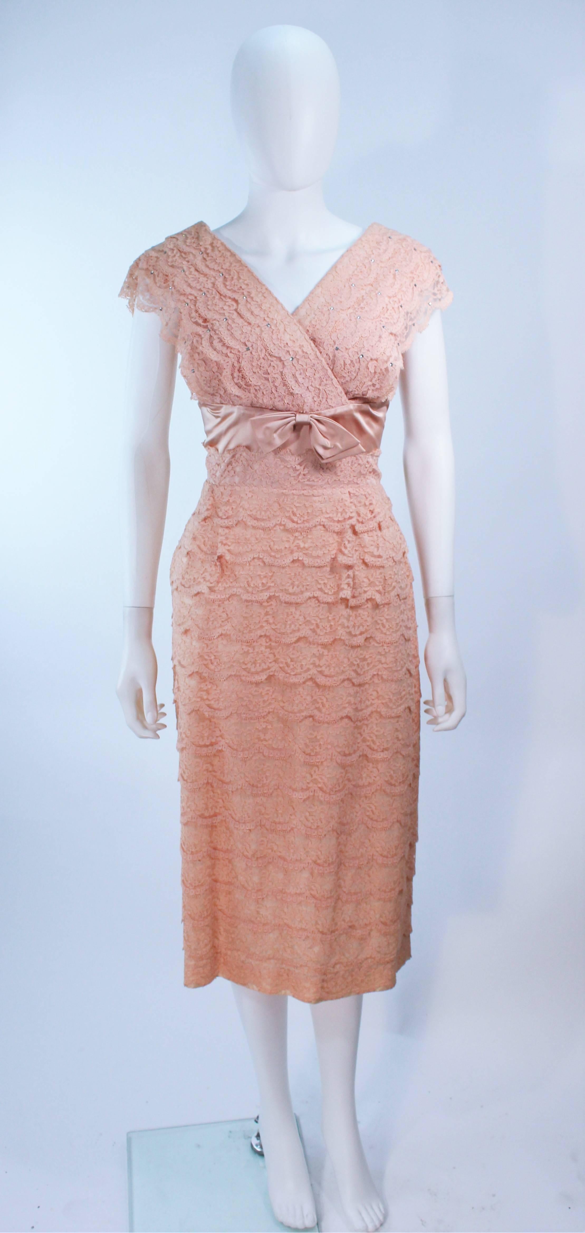  This cocktail dress is composed of a peach hue lace with tiered scalloped edges and rhinestone applique at the bust. Features a satin waist with bow. There is a center back zipper closure. In great vintage condition.

  **Please cross-reference