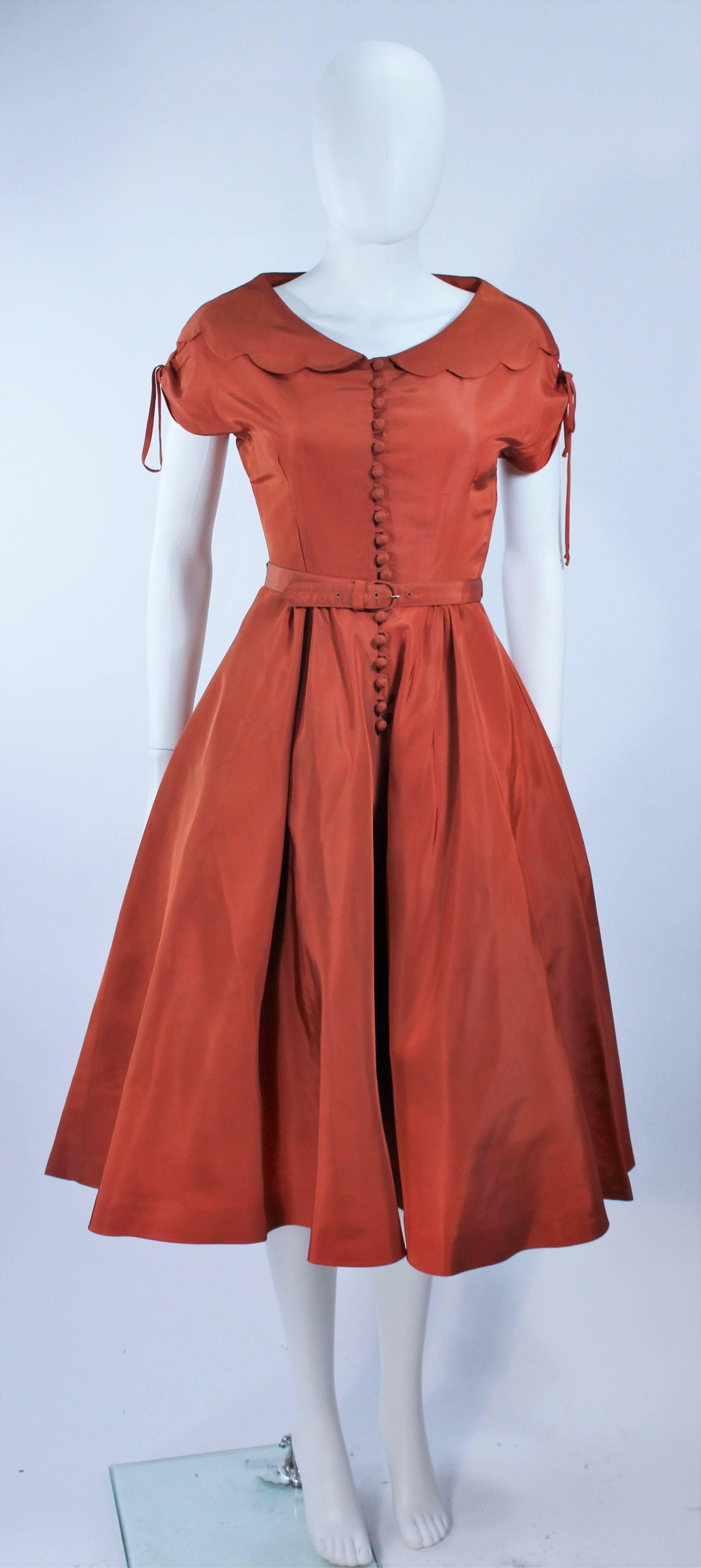 This cocktail dress is composed of a burnished orange taffeta. Features scalloped edges with center front button closures and belt. In excellent vintage condition, small spot on back (see photo). Shown with crinoline (sold separately).

**Please