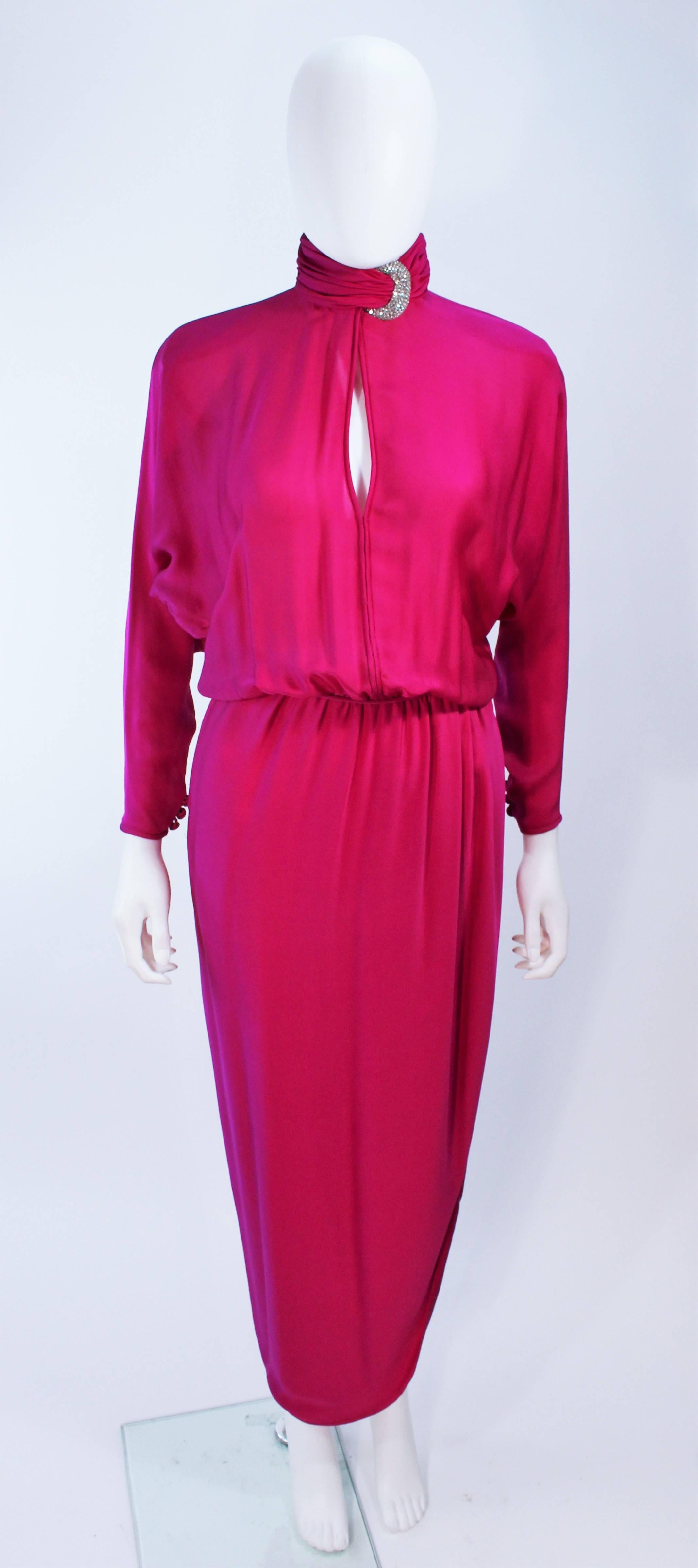 This Galanos attributed gown is composed of a magenta silk and feature rhinestone buckle accents (at the collar and waist). Features a side slit with mock collar. There are side closures and buttons at the cuff. In excellent vintage condition, some