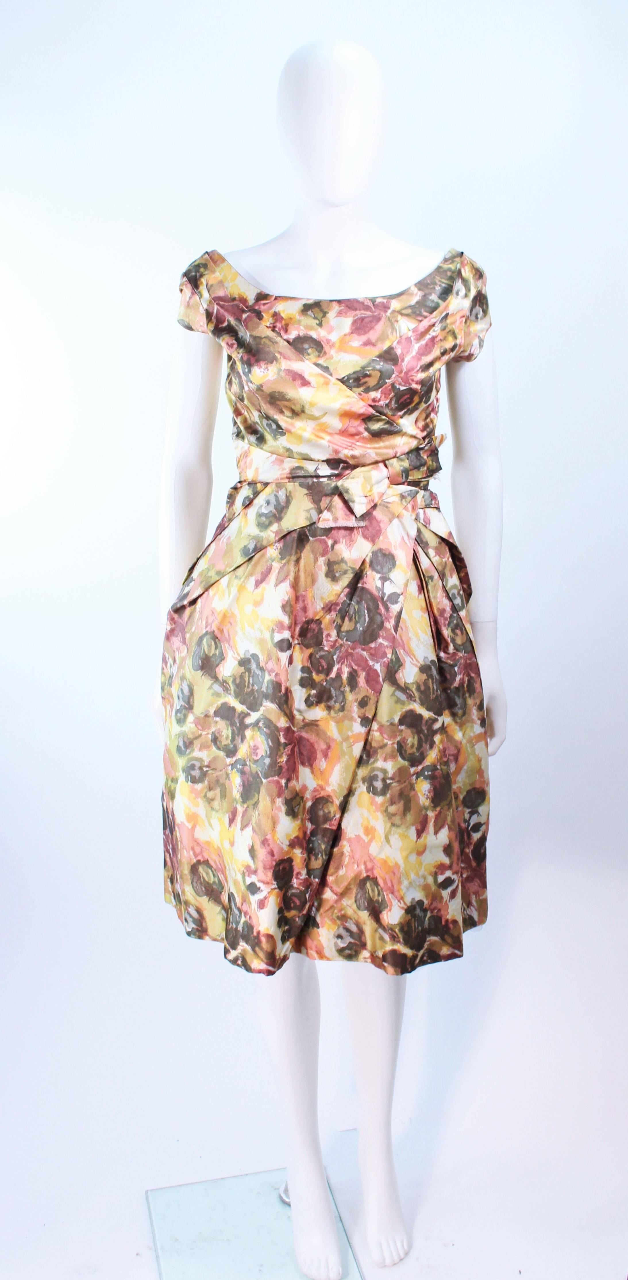 This vintage cocktail dress is composed of a floral watercolor pattern silk in Earth tone hues. Features a draped bow design at the waist. There is a center back zipper closure. (The cocktail dress, due to its small size, was unable to completely