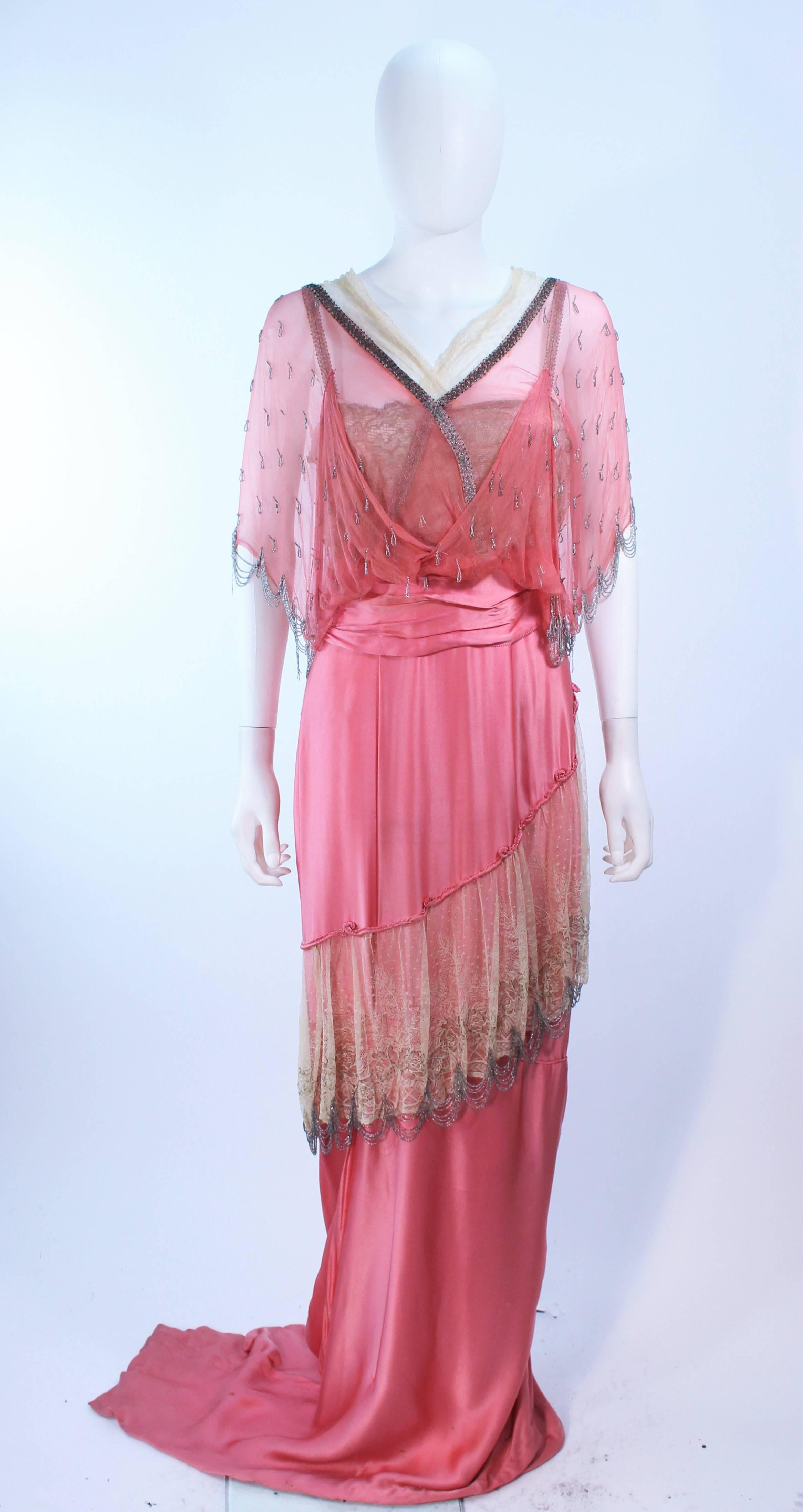 This Victorian gown is composed of a pink silk with lace trim and a beaded applique throughout. Features a drape style with chiffon. There are hook and eye closures with snaps. In antique vintage condition, there is discoloration and deterioration