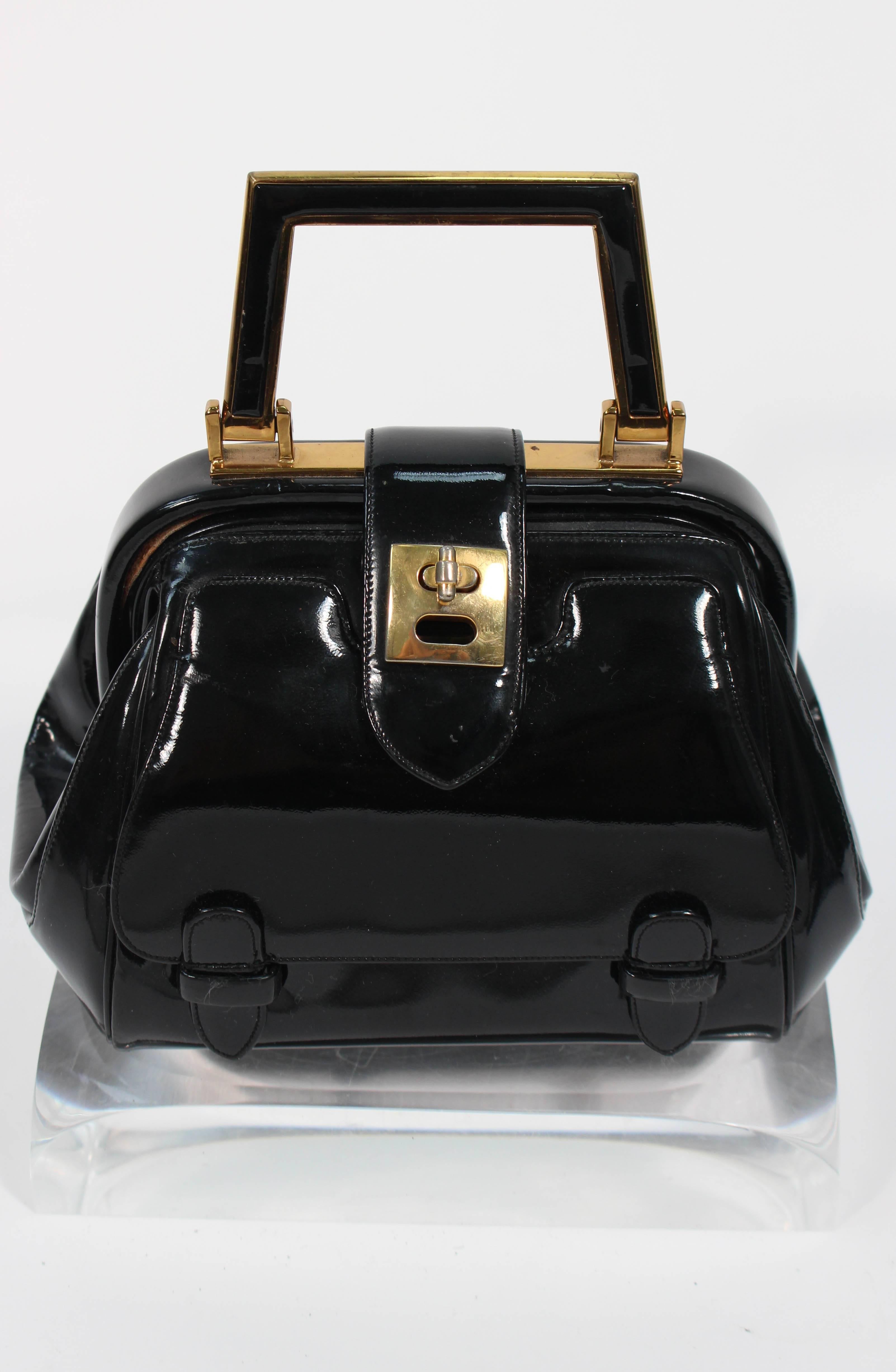 This Judith Leiber handbag is composed of a black patent leather with gold tone hardware. It is a very rare 1960's design featuring turn style closures with an exterior pocket. There are interior compartments with a silk lining. In excellent vintage
