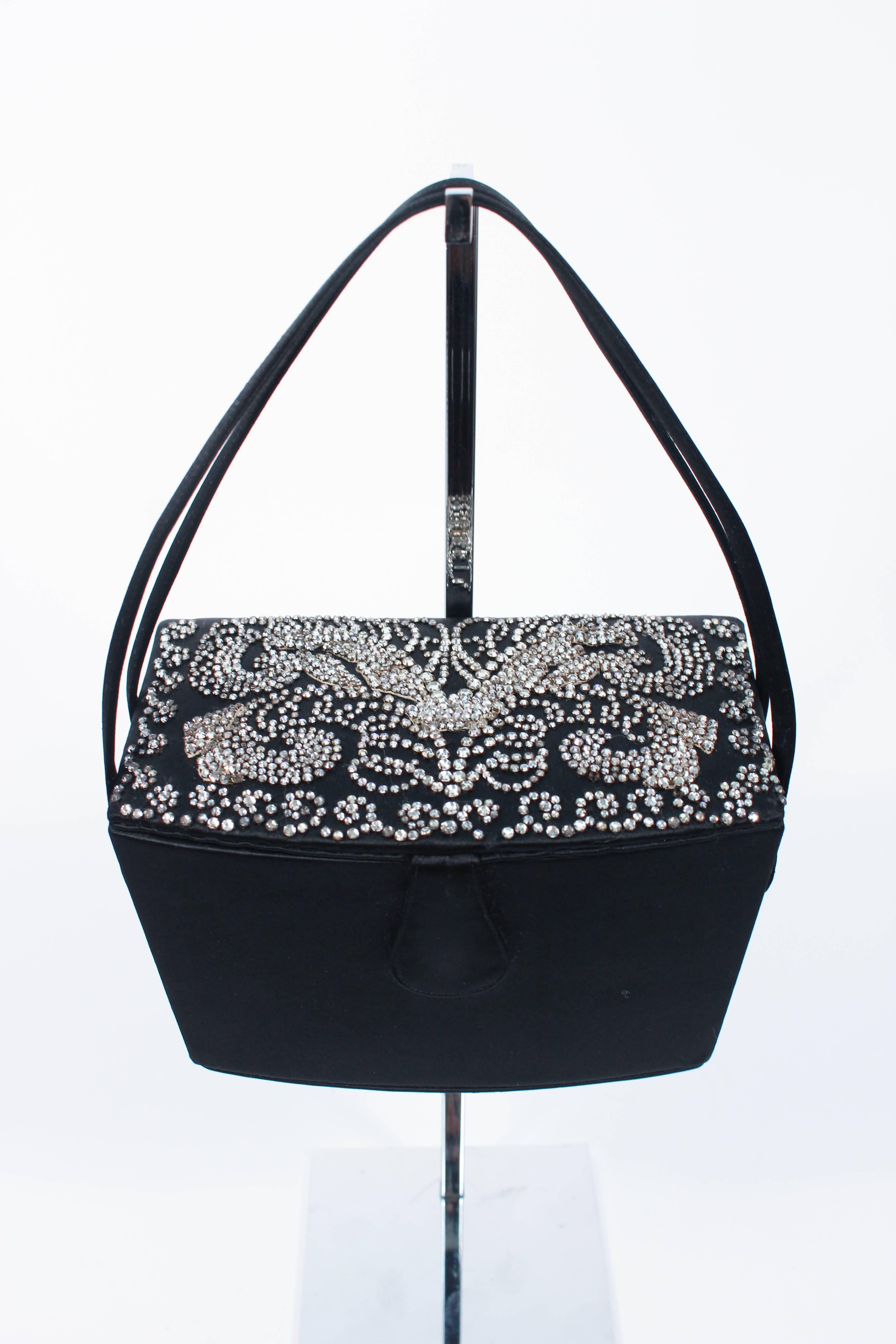 This vintage Josef purse is composed of a black silk satin. Features an intricate rhinestone rhinestone applique top. Comes with a rhinestone pen, wallet, and miniature mirror. There is an interior compartment with silk lining and mirrored interior