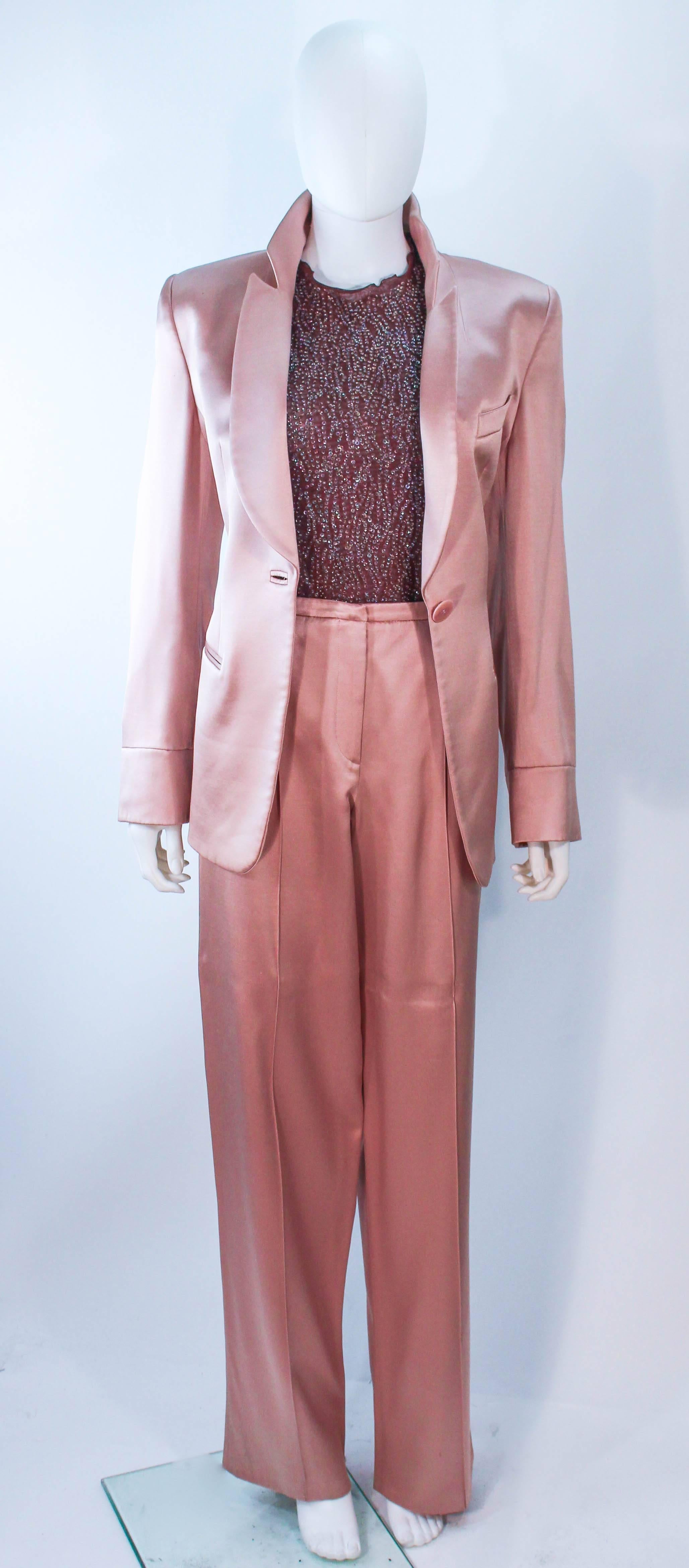 Cette combinaison pantalon Giorgio Armani est composée d'une soie de teinte rose mauve, accompagnée d'un body en maille perlée marron. La veste se ferme par un bouton central sur le devant et le pantalon se ferme par une fermeture éclair. En parfait