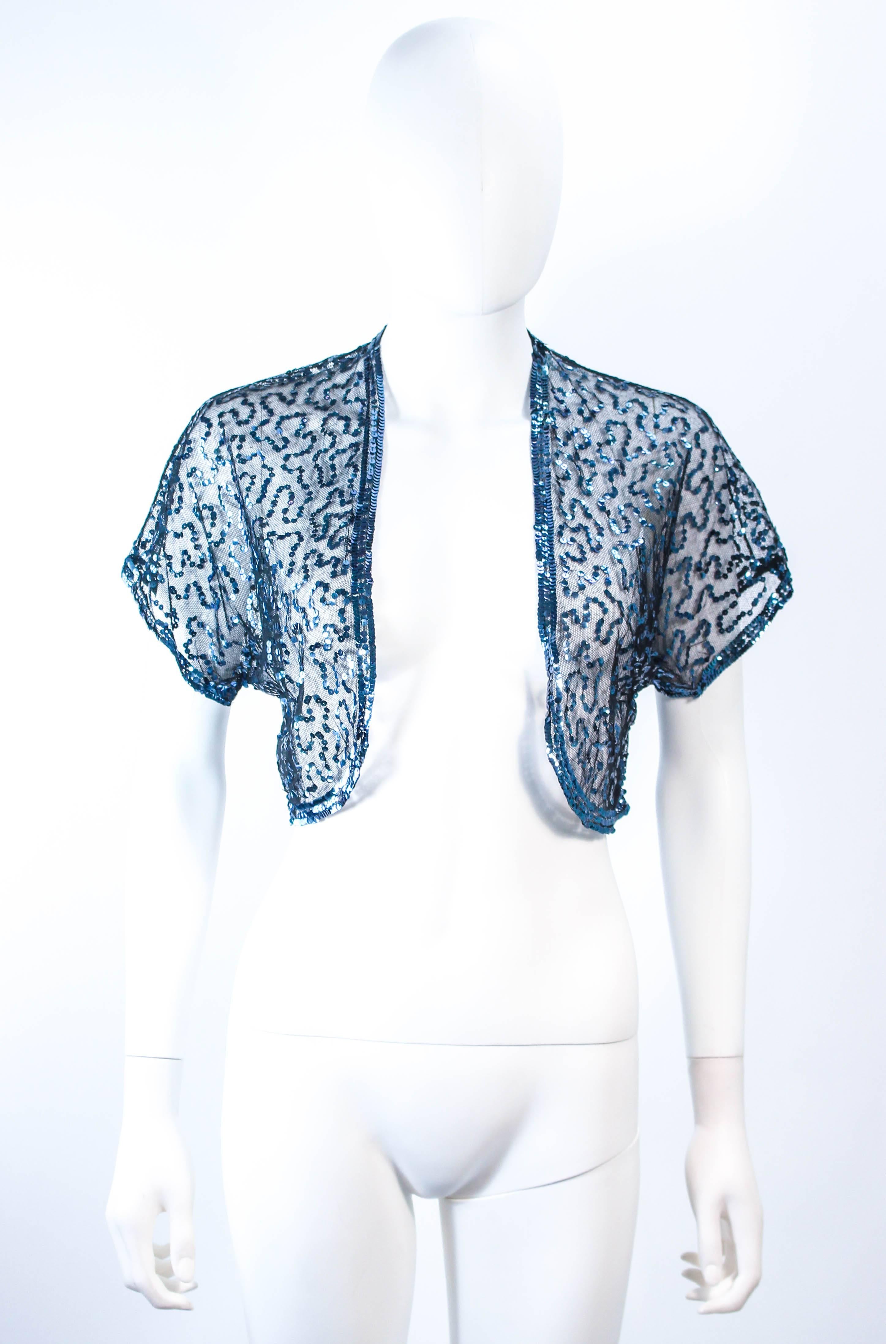 Esta chaqueta antigua está compuesta por una malla negra transparente con apliques de lentejuelas azules. Presenta un estilo abierto. En excelente estado vintage. 

**Por favor, coteje las medidas para mayor precisión personal. El tamaño en el