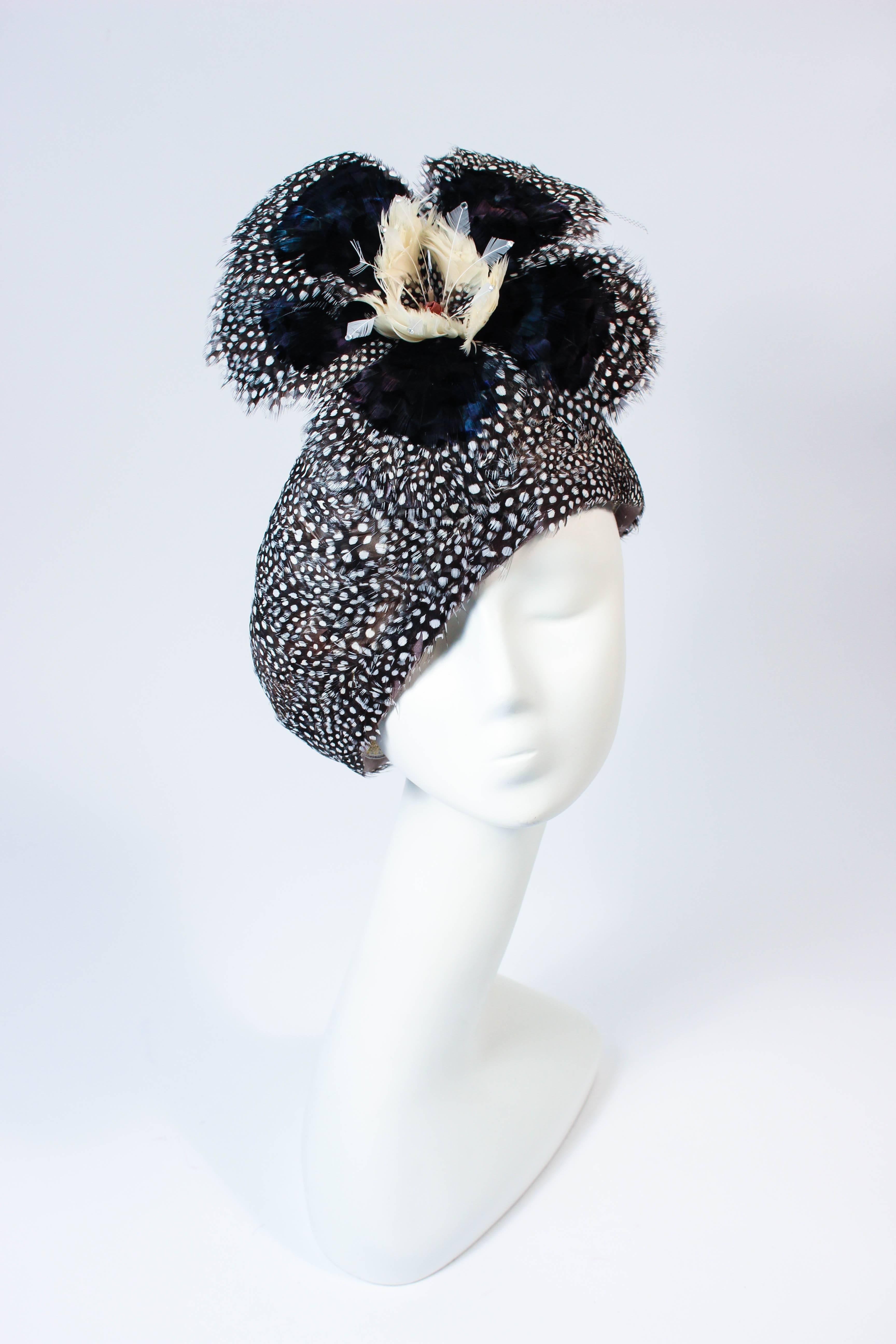 This Jack McConnell hat s composed of a stunning array of feathers in navy and cream hues with petite spotted feathers. Features a large flower with rhinestone applique. In excellent vintage condition.

**Please cross-reference measurements for