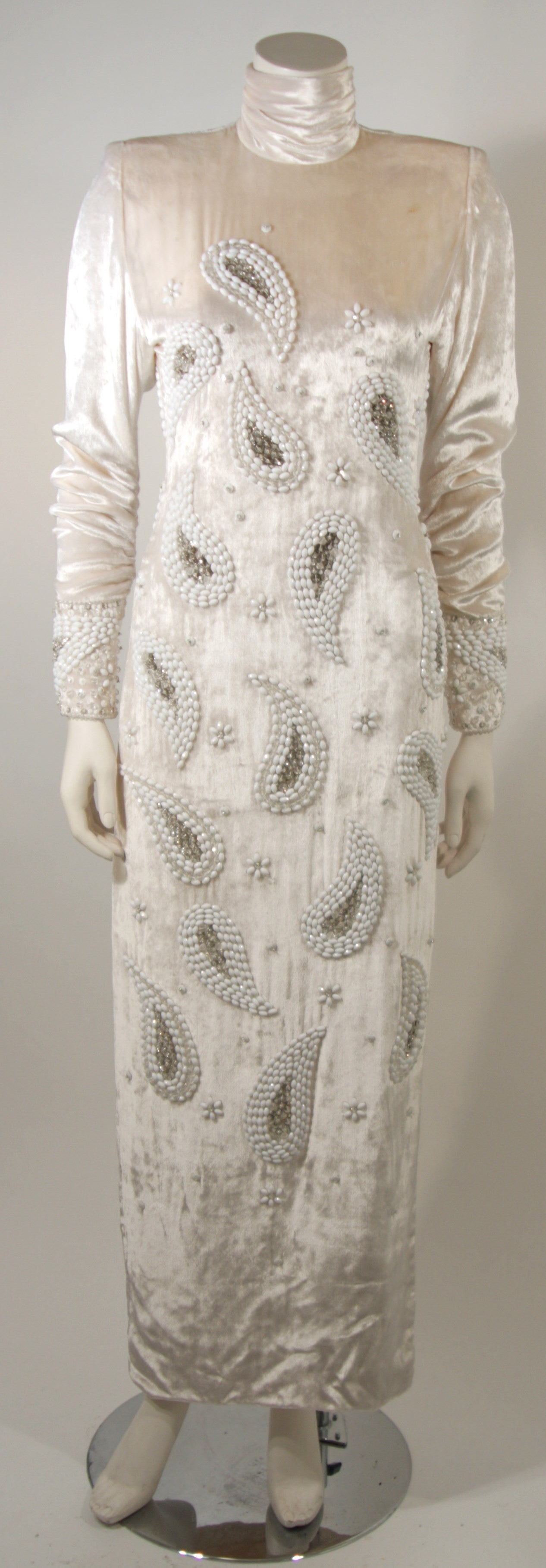 This Galanos gown is available for viewing at our Beverly Hills Boutique. The dress is composed of an off white crushed velvet and features ornate embellishments. Beautiful ruching at the neck and sleeves. There is a center back zipper and zippers