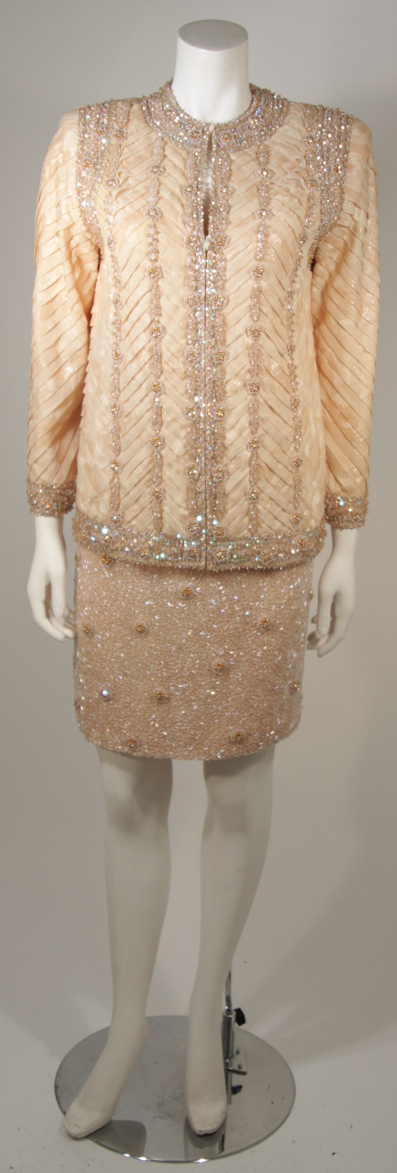 This Galanos suit is available for viewing at our Beverly Hills Boutique. The set is composed of a metallic bronze and peach silk organza, hand beaded with iridescent beads and rhinestones. The jacket features a center front zipper closure and the