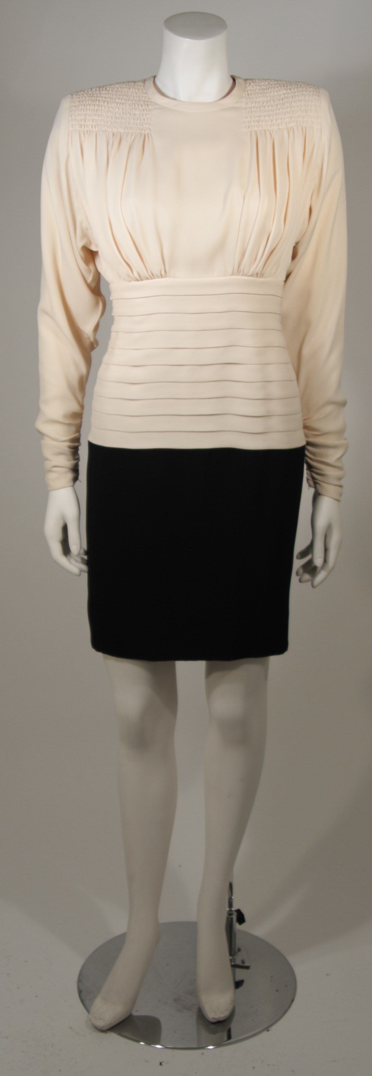 This cocktail dress attributed to Galanos is available for viewing at our Beverly Hills Boutique. The dress is composed of a black and ivory contrasting silk combination. The dress features smocking at the shoulders, pleating at the waist, and