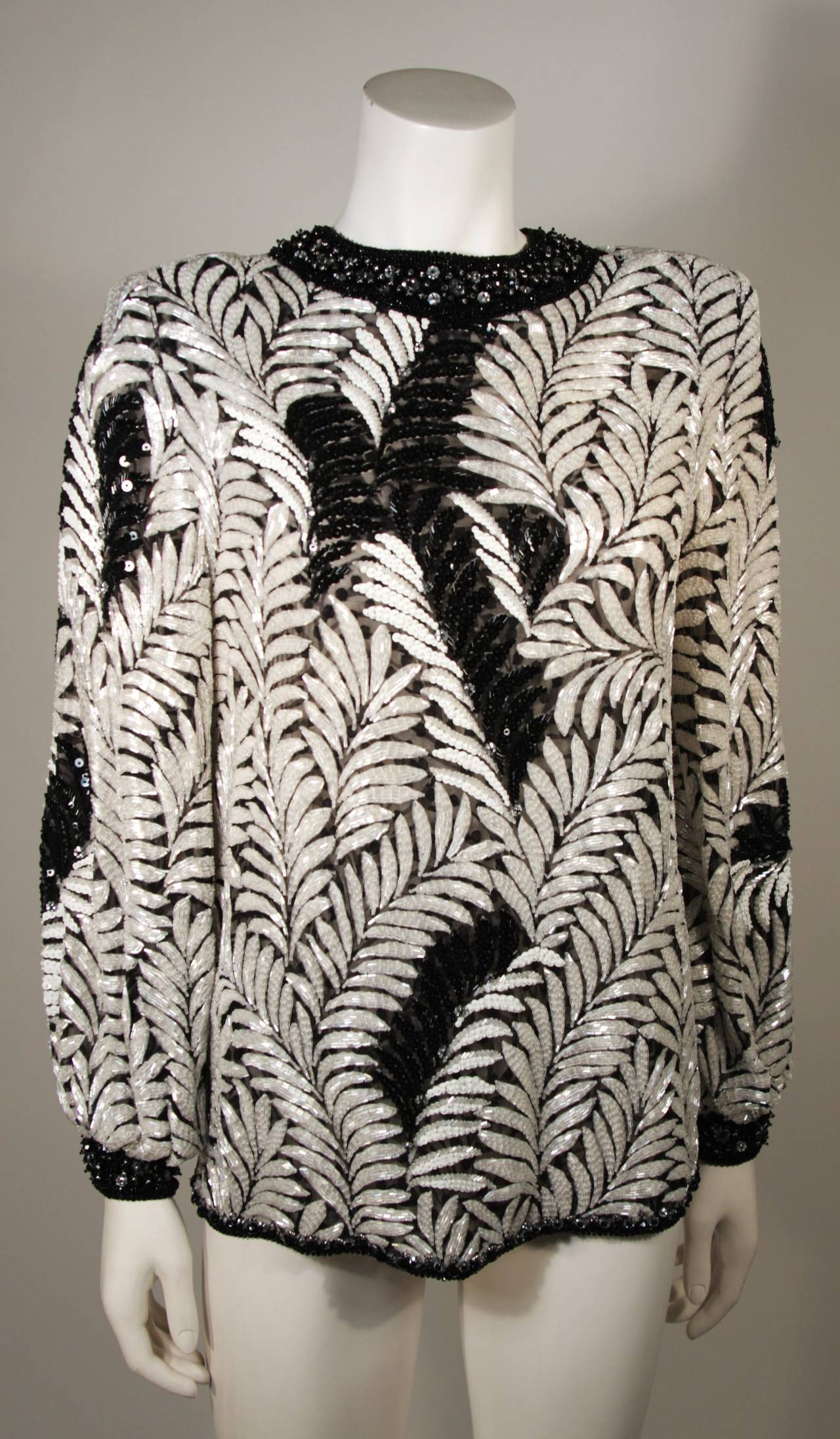This Galanos blouse is available for viewing at our Beverly Hills Boutique. The top is composed of a wonderfully embellished Palm motif fabric. The ornate embellishment is brought to life with the black and white contrasting beading. There is a