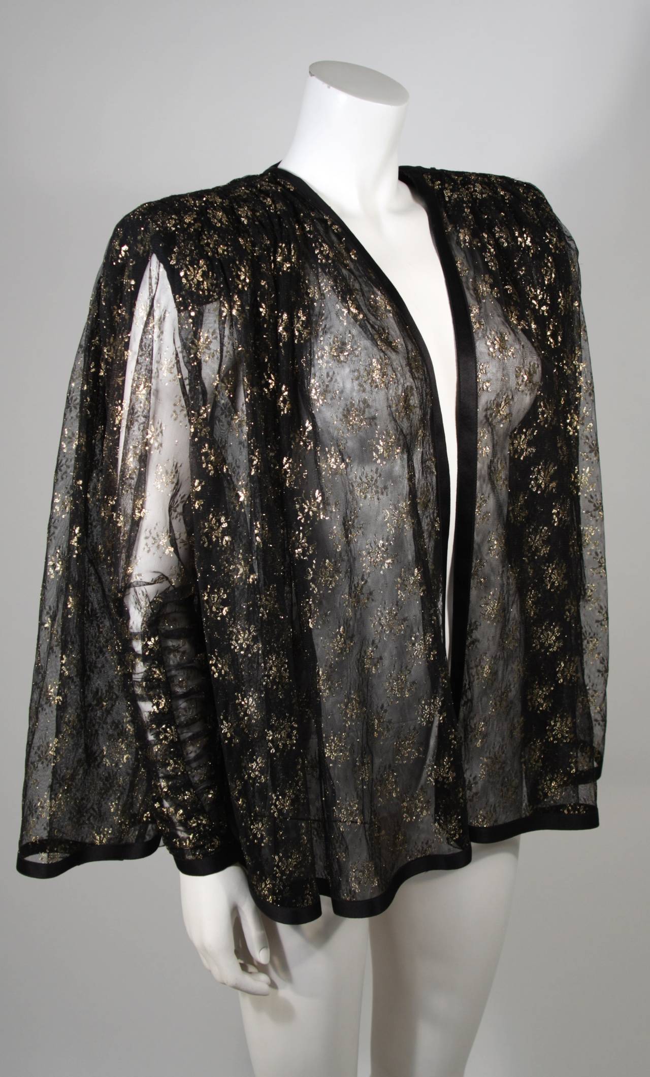 This design attributed to Galanos is available for viewing at our Beverly Hills Boutique. This dramatic multi-layered piece is fashioned from the finest sheer black fabric with gold metallic accents. The sleeves feature a zipper and are ruched. This