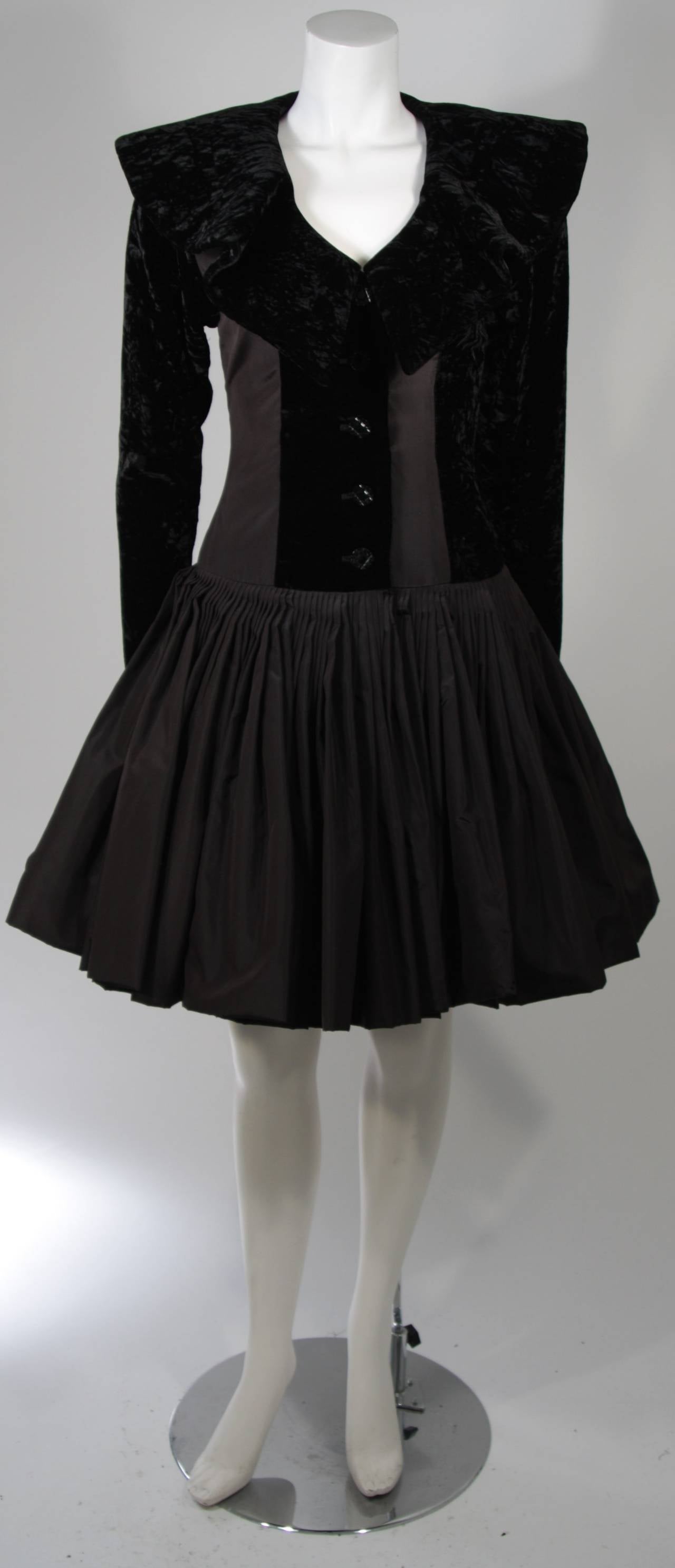 This wonderful Galanos Design is available for viewing at our Beverly Hills Boutique. The dress is fashioned out of black silk and velvet. The large and dramatic collar is accented by a flattering full gathered skirt. There are center front snap and