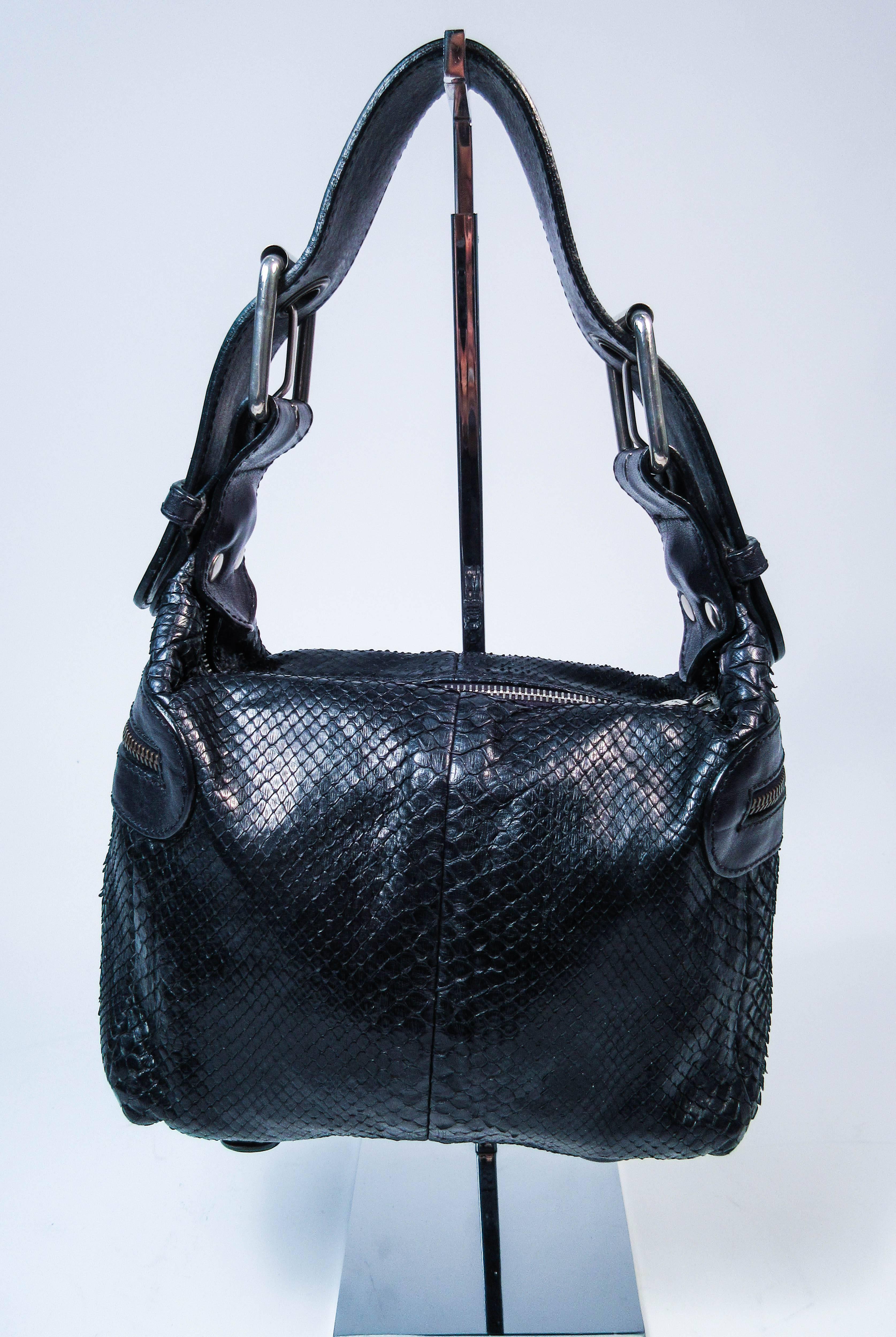 This Chloe purse is composed of black python skin and features a top handle with buckle accenting. There are two exterior zipper compartments and one interior zipper compartment. In excellent pre-owned condition (some signs of wear due to