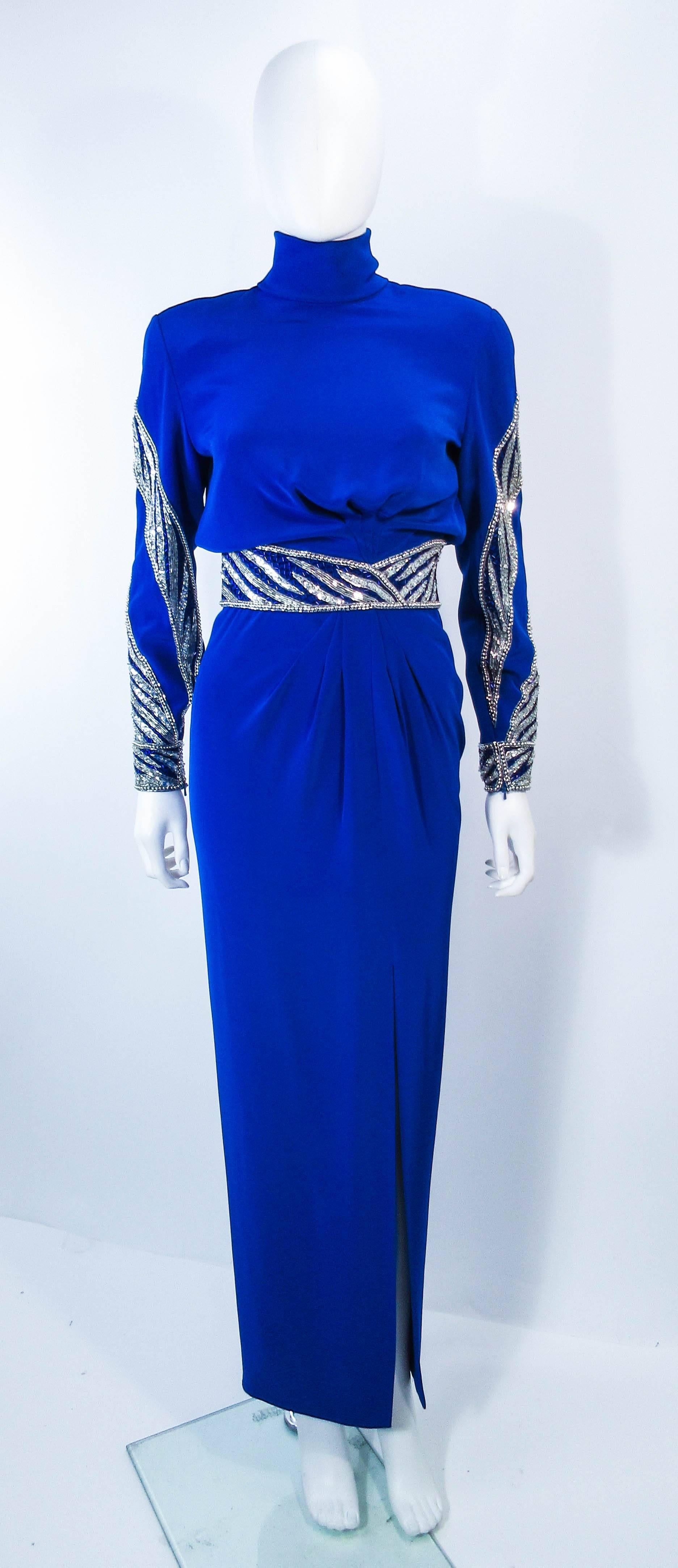 This vintage Bob Mackie gown is composed of a royal blue fabric with beaded trim and applique. Features a mock neck with center back zipper closure and side slit. In excellent vintage condition.

  **Please cross-reference measurements for personal