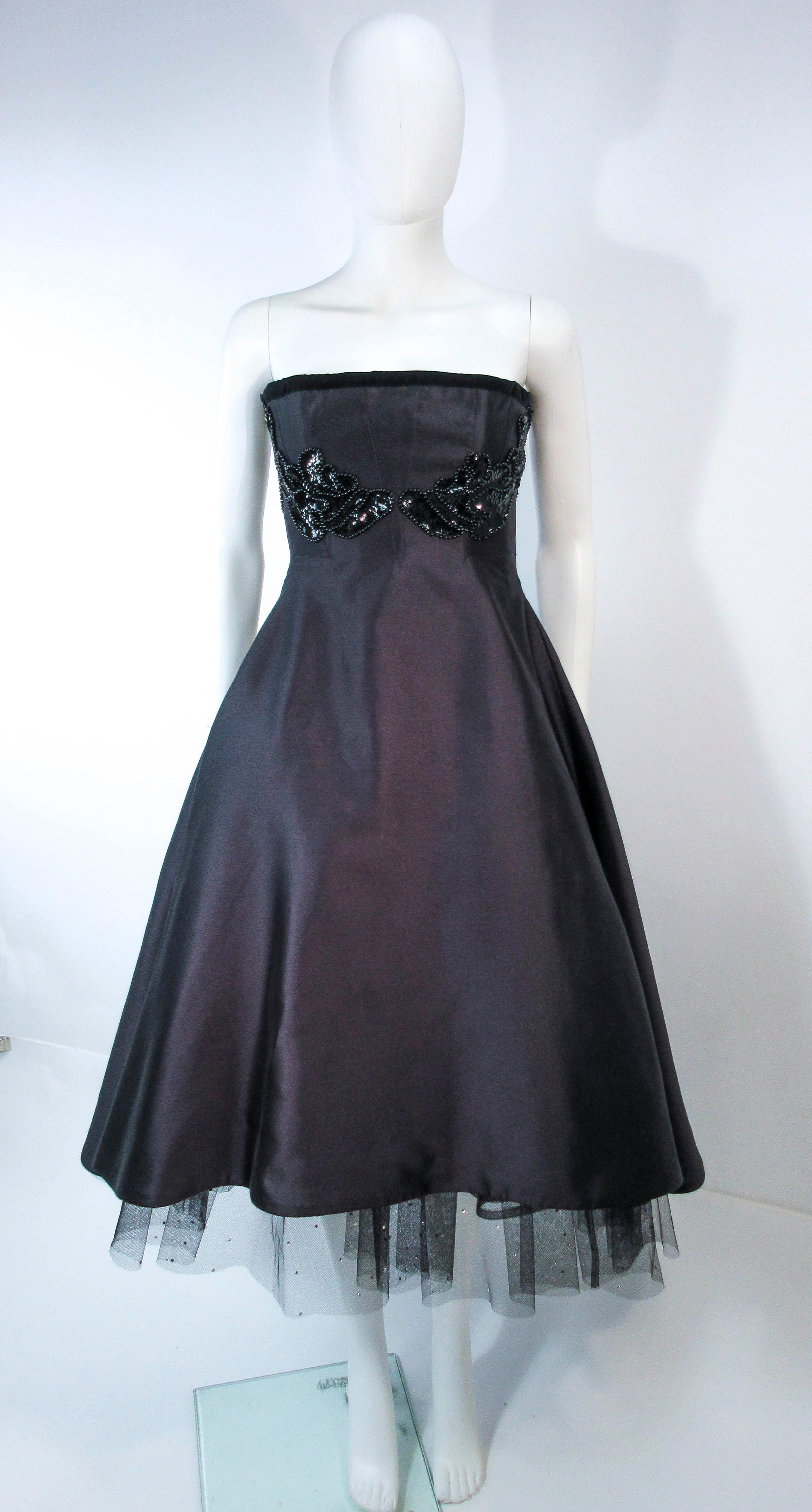 This Elizabeth Mason Couture design is a vintage redesign. The cocktail dress is composed of a black silk and features an interior bustier with boning. The crinoline features a splash of rhinestone embellishments for a fabulous pop. This one of a