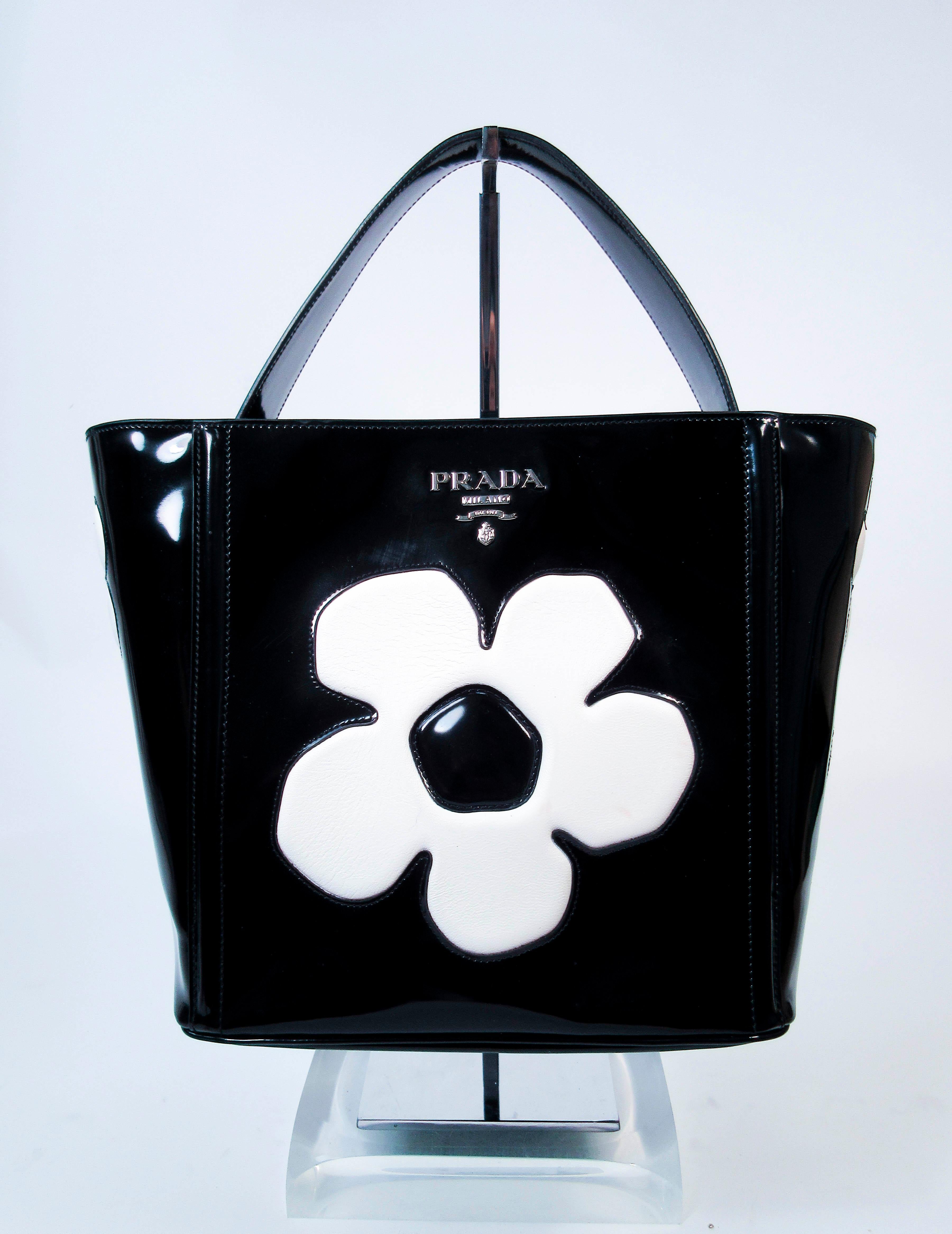 This vintage Prada purse is composed of black & white patent leather. Made in Italy. Features multiple interior compartments & an optional strap. Comes with dustbag. In excellent 